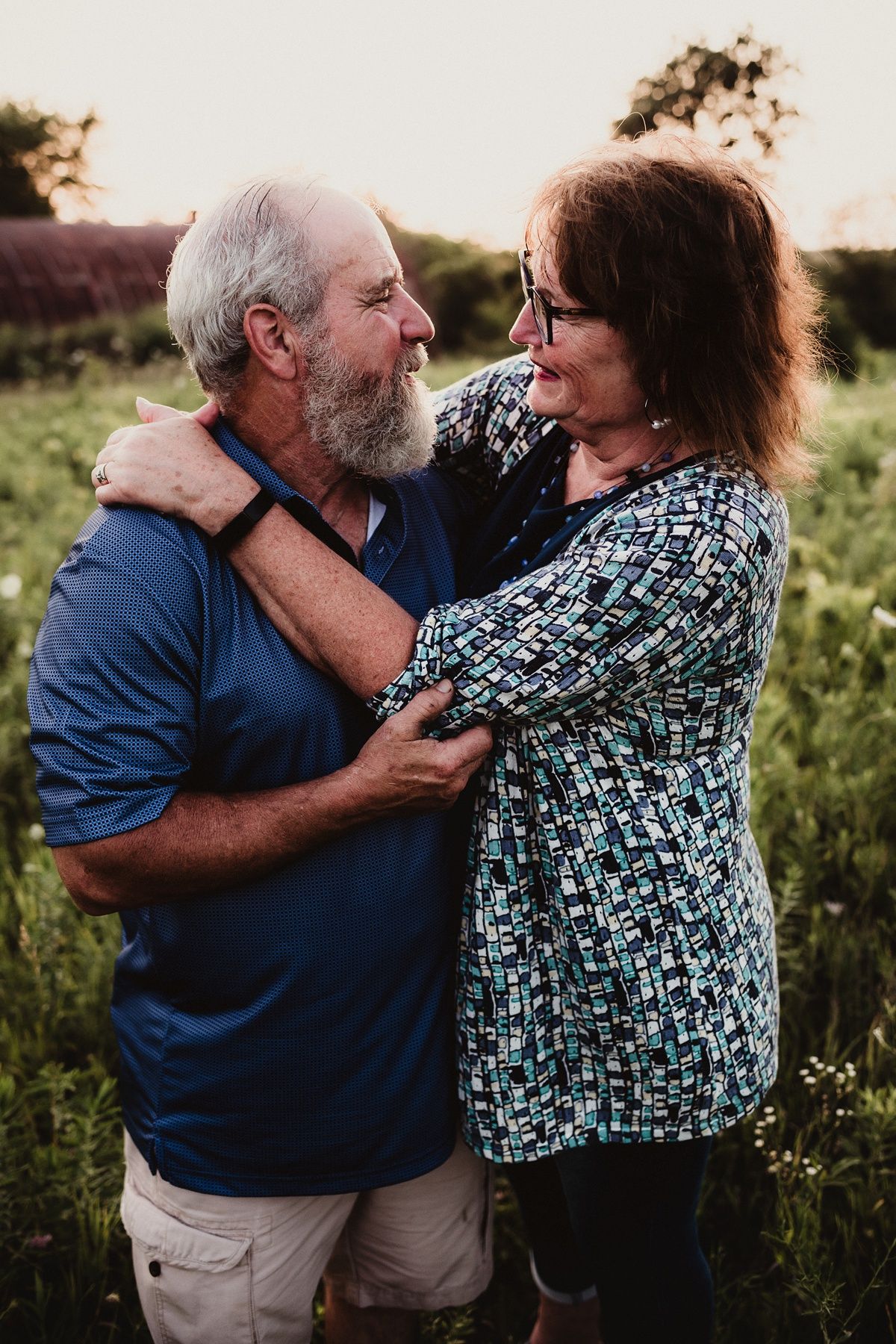 A senior couple shares an affectionate moment while laughing together in a meadow at sunset.
