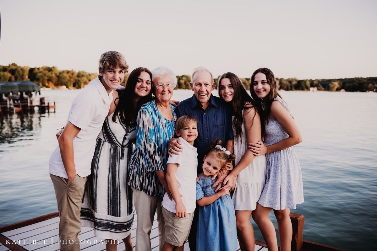 Group portrait of family members standing together on dock by lake at sunset.