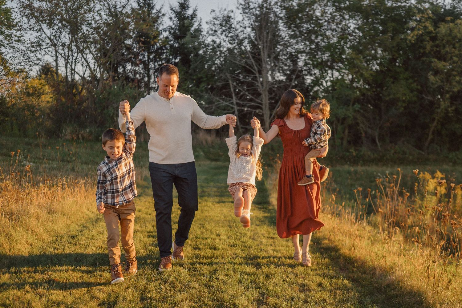 A group walks together through a golden meadow at sunset with tall grass and trees in the background.