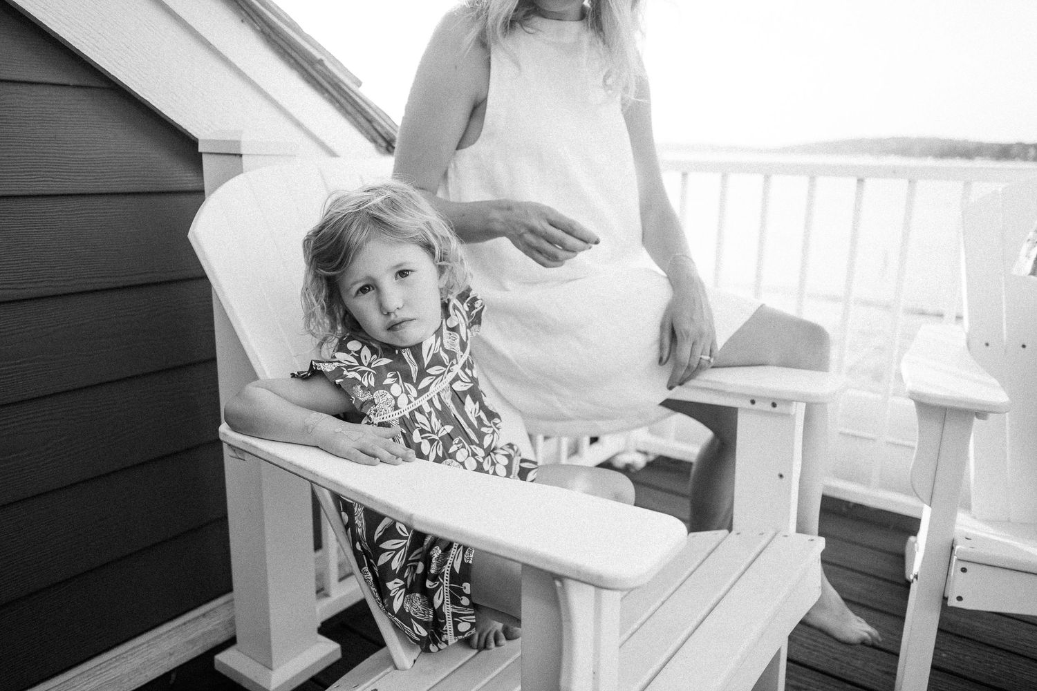 People relax in white Adirondack chairs on a sunny porch.
