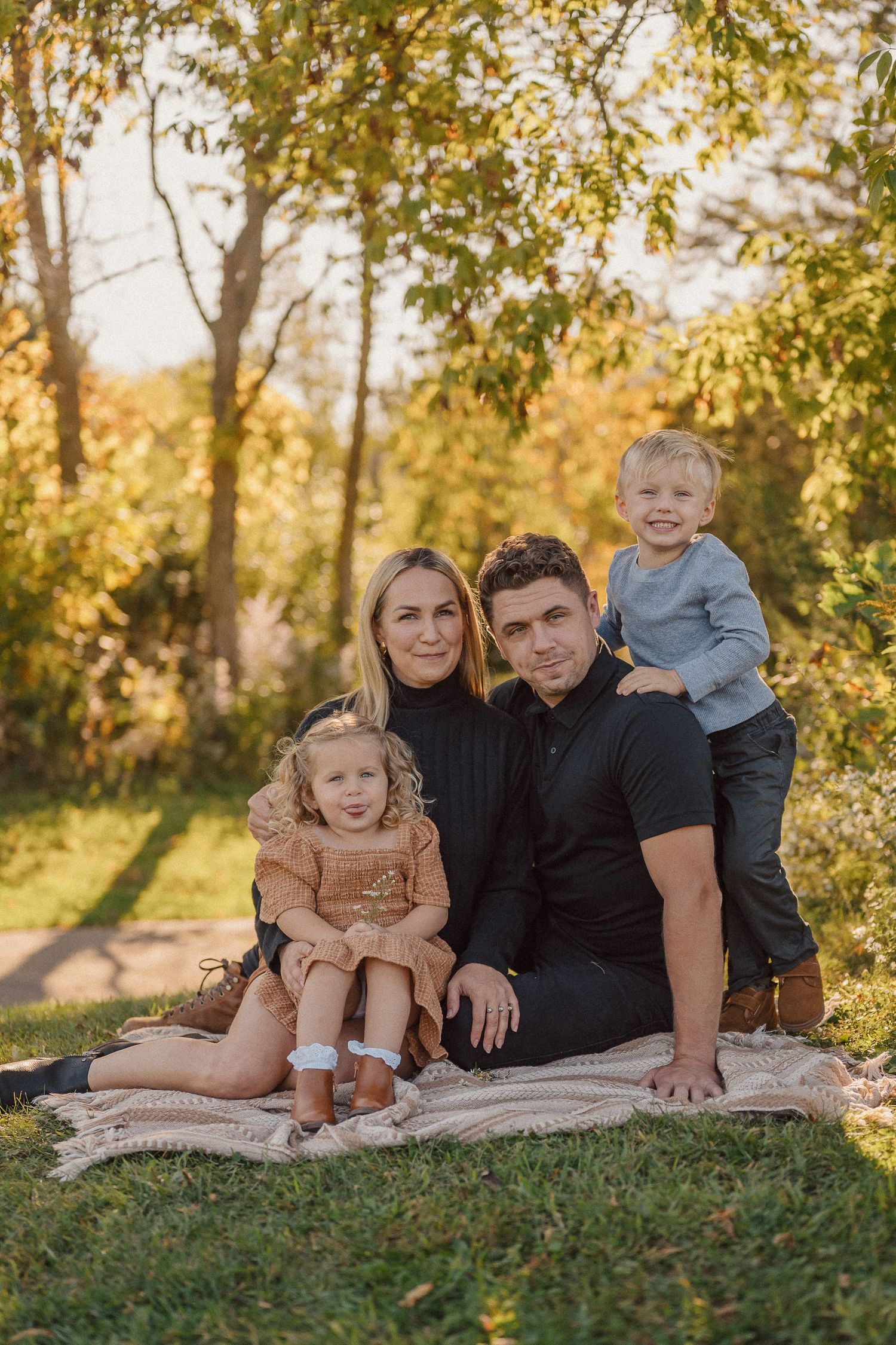 Family portrait on blanket with autumn trees and golden sunlight in background.