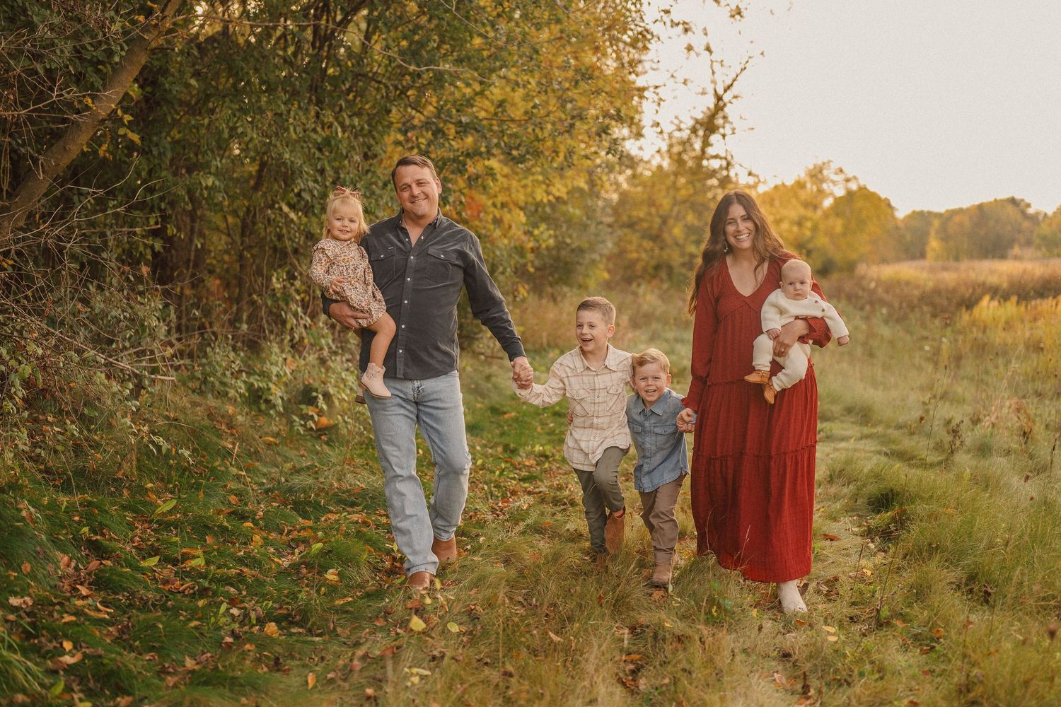 Family walking together through a golden autumn field at sunset during a lifestyle photography session.