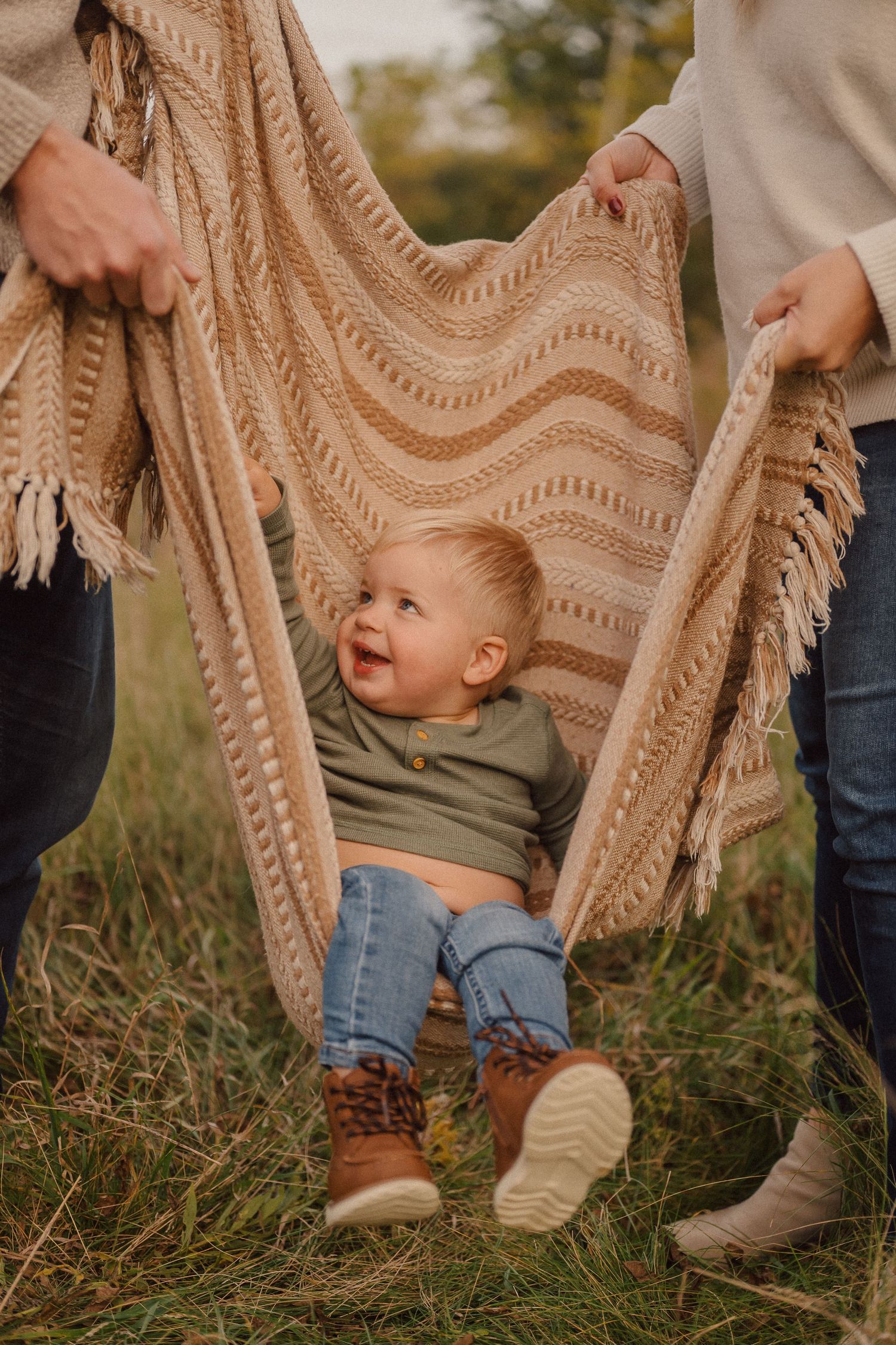 Close-up of small feet and a textured blanket in grass during outdoor family photoshoot.