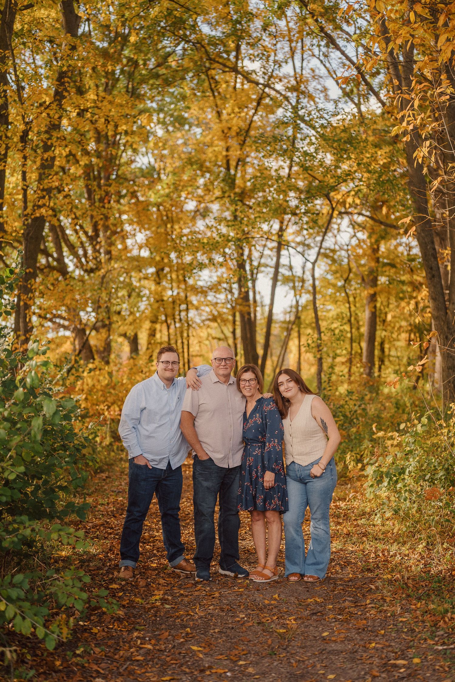 A group stands together on a leaf-covered path surrounded by golden autumn trees in warm evening light.