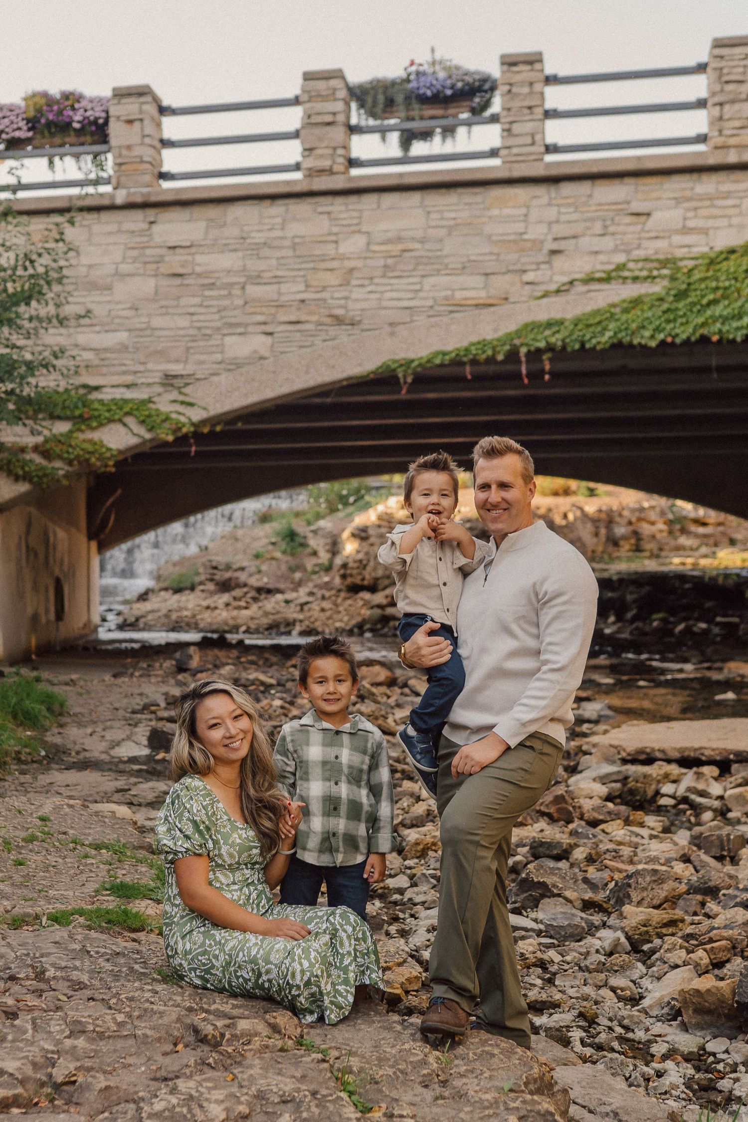 Family sitting together under a stone bridge near a rocky creek bed.