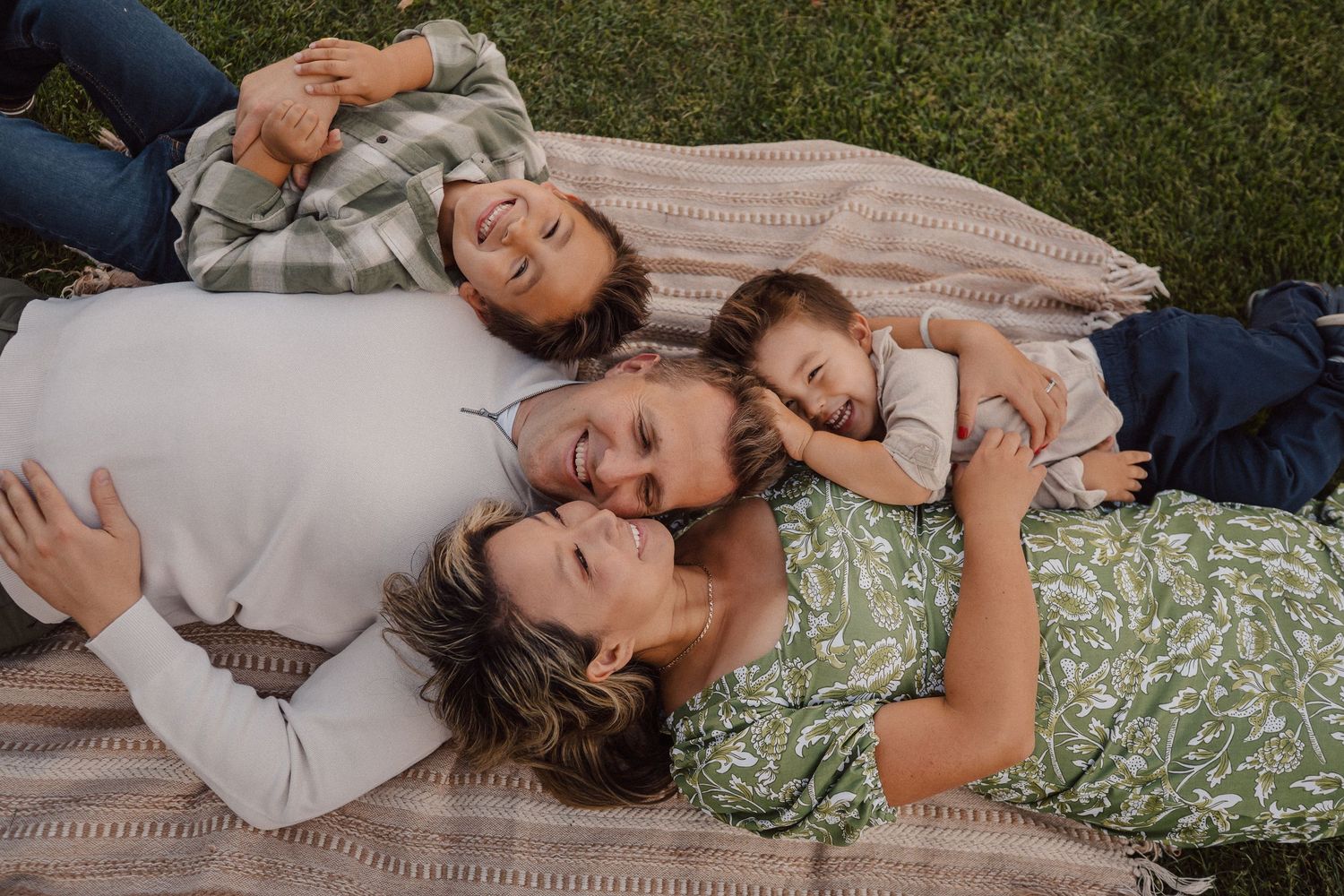 A candid family moment lying together on a picnic blanket in a grassy outdoor setting.
