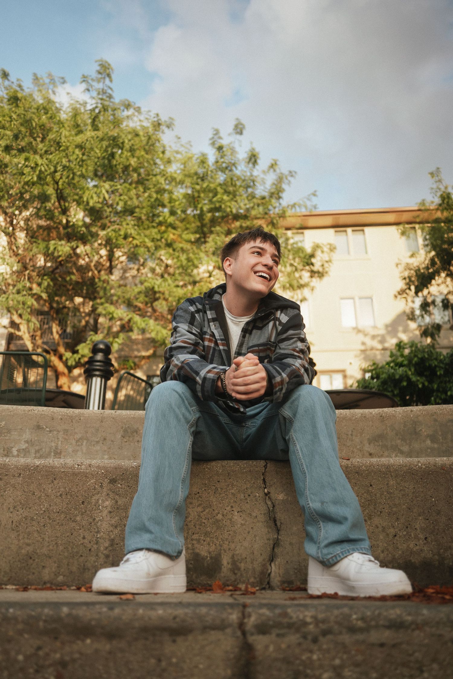 A candid shot of someone sitting on outdoor steps wearing a camo jacket and white sneakers against an urban backdrop.