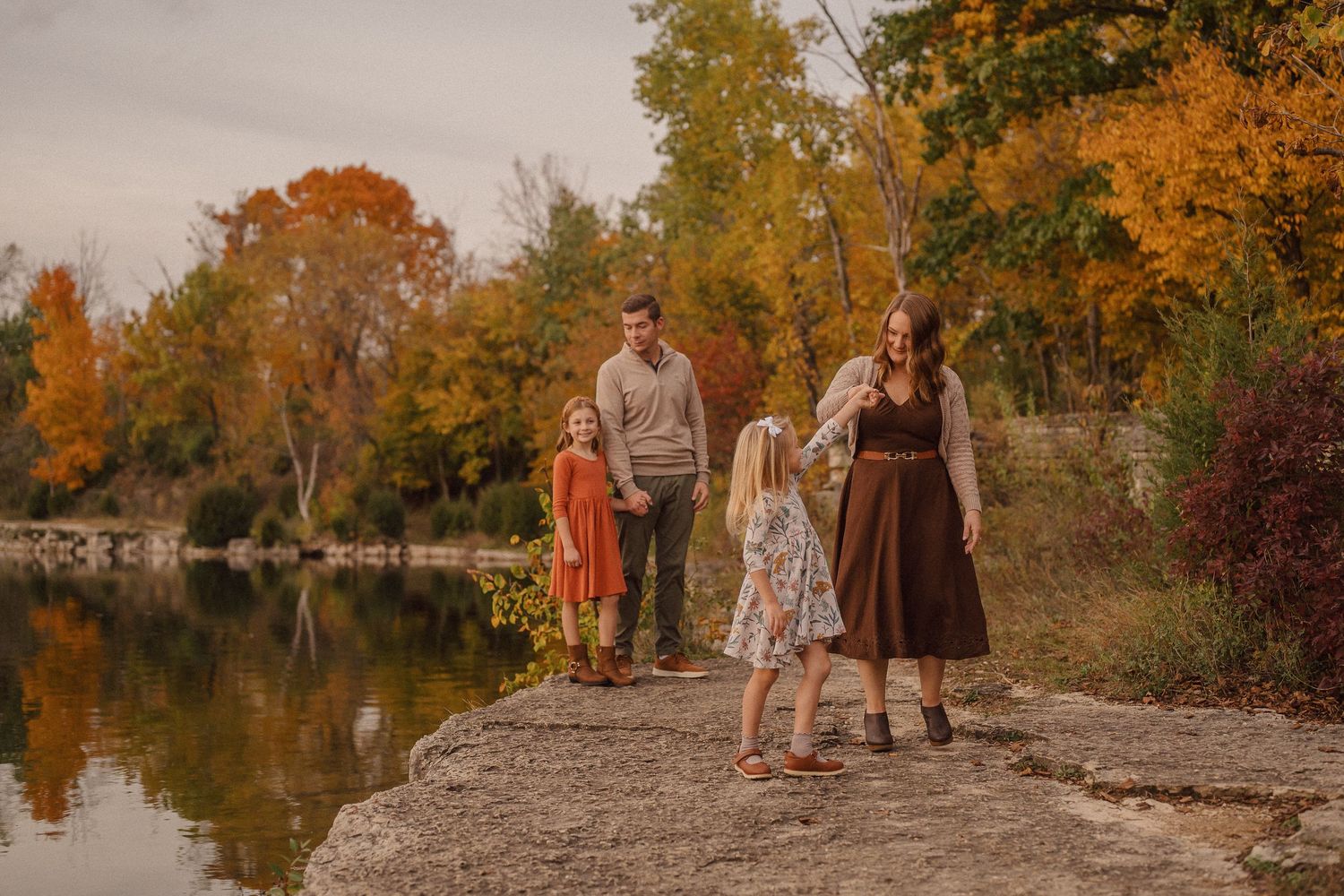 Family enjoying a scenic autumn photoshoot by a tranquil lake with golden foliage reflecting in the water.