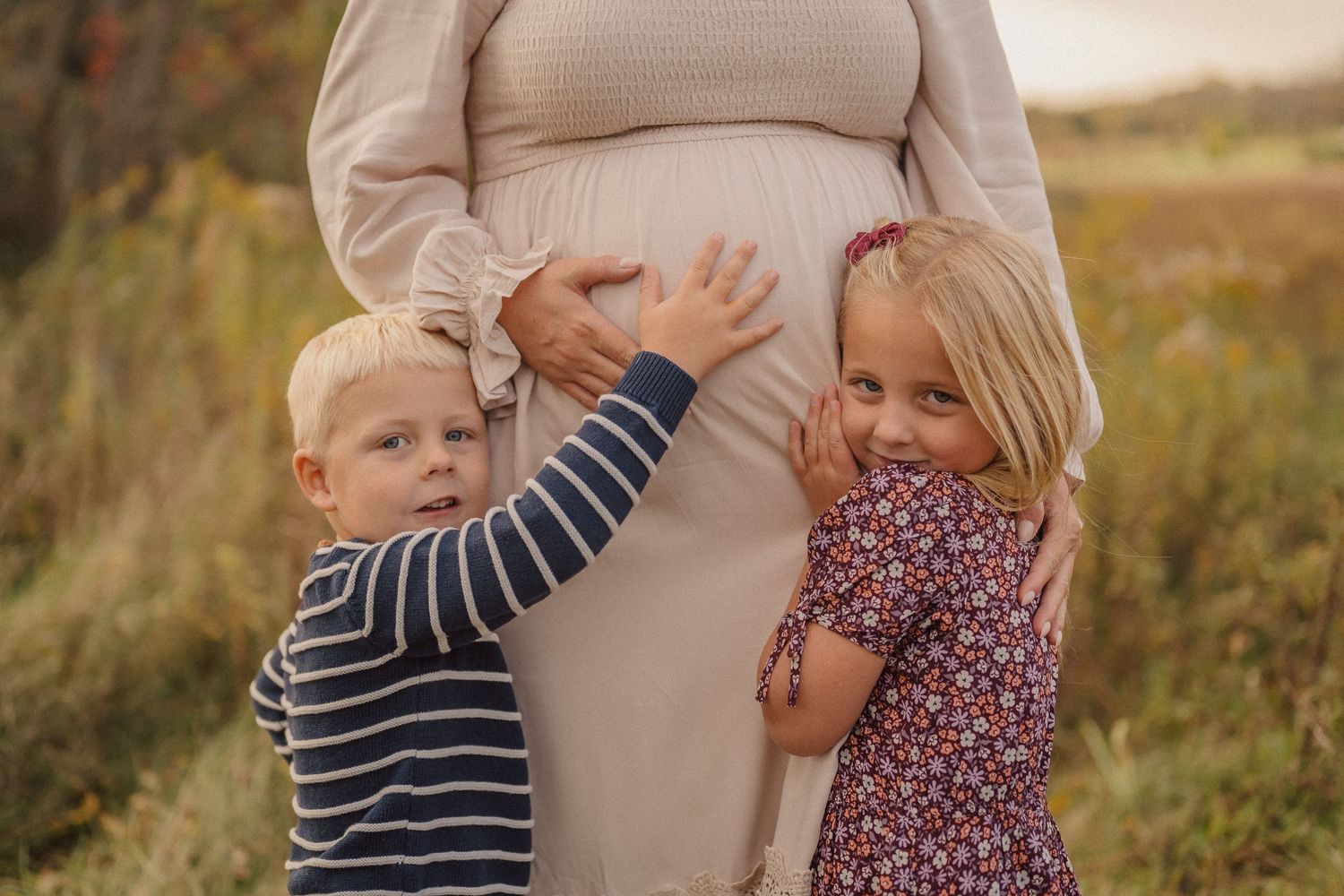 Expecting mother shares tender moments with children in autumn field setting.