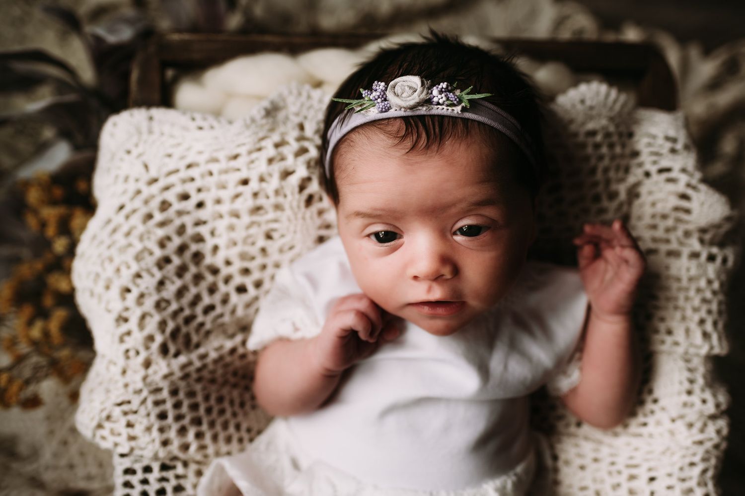 Baby wearing sparkly crown headpiece while lying on cream knit blanket.