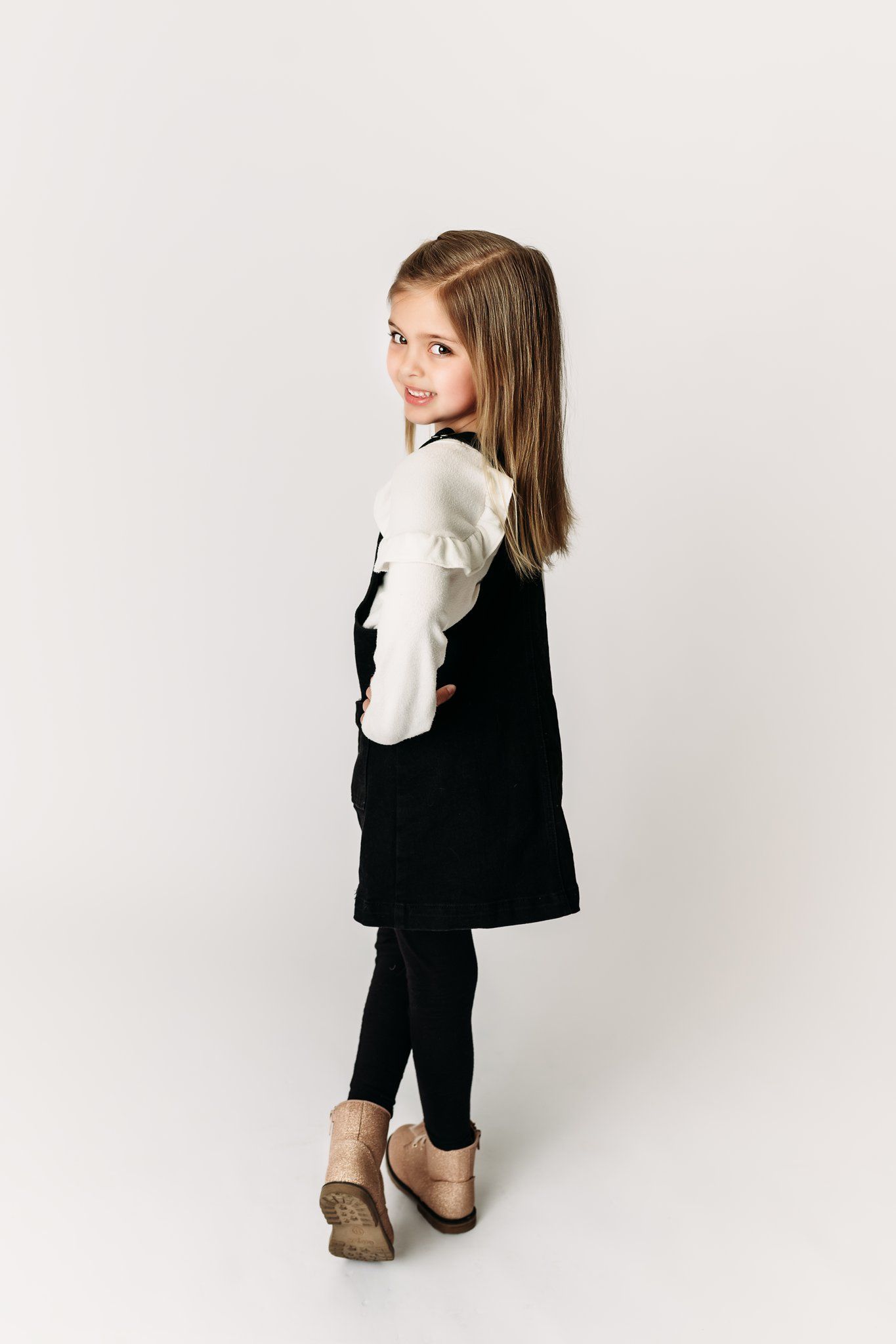 Back view of child in black jumper dress and white shirt looking over shoulder.