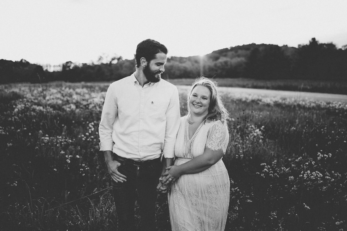 Candid couple laughing together in a sunlit field with wildflowers.