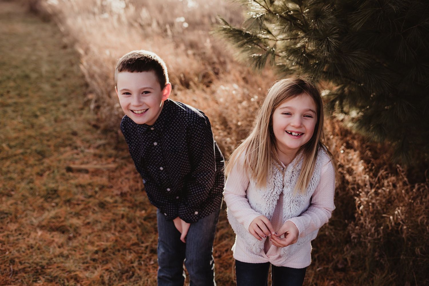 Two children laughing and posing together on an autumn path.
