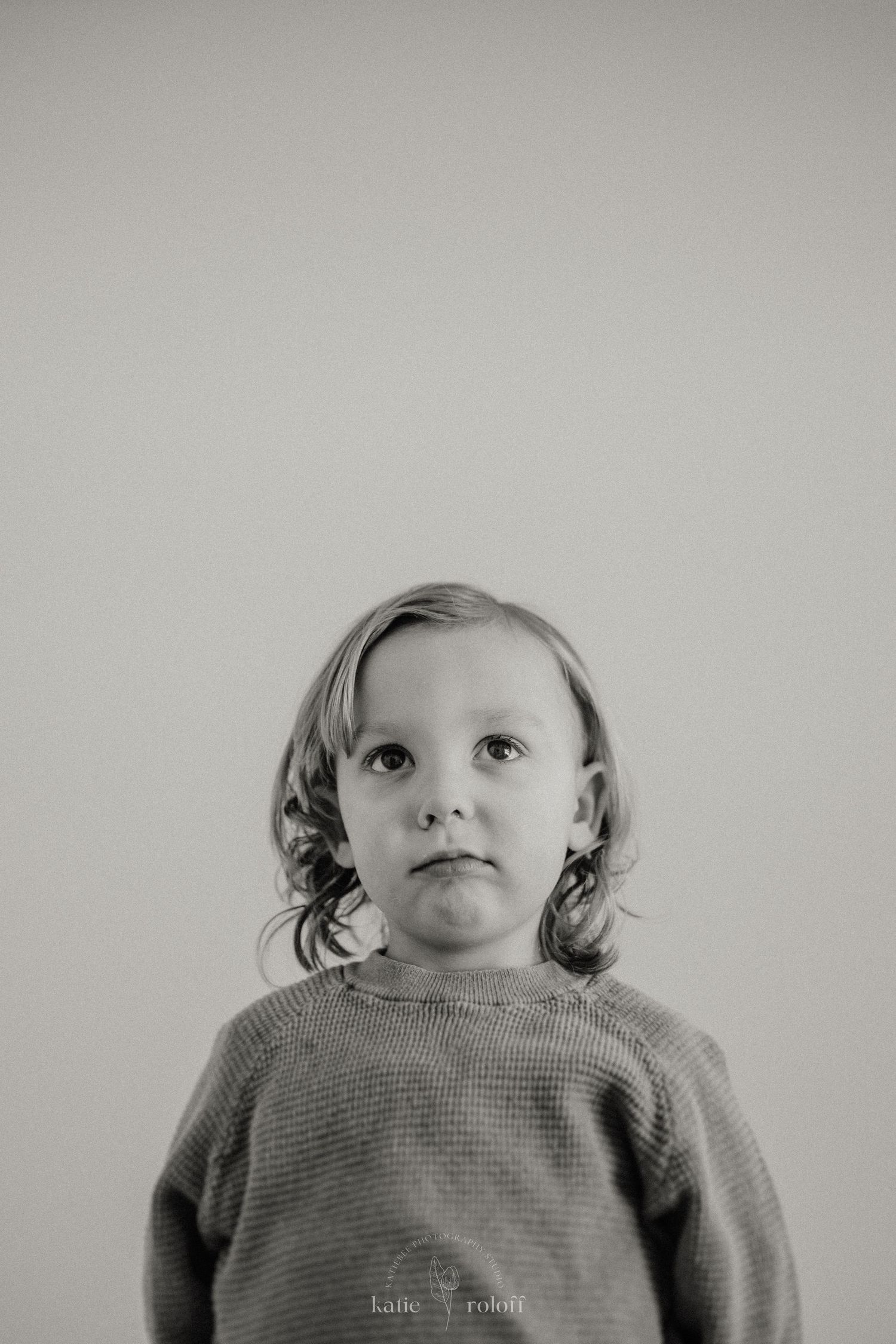 A minimalist black and white portrait against a light gray background.
