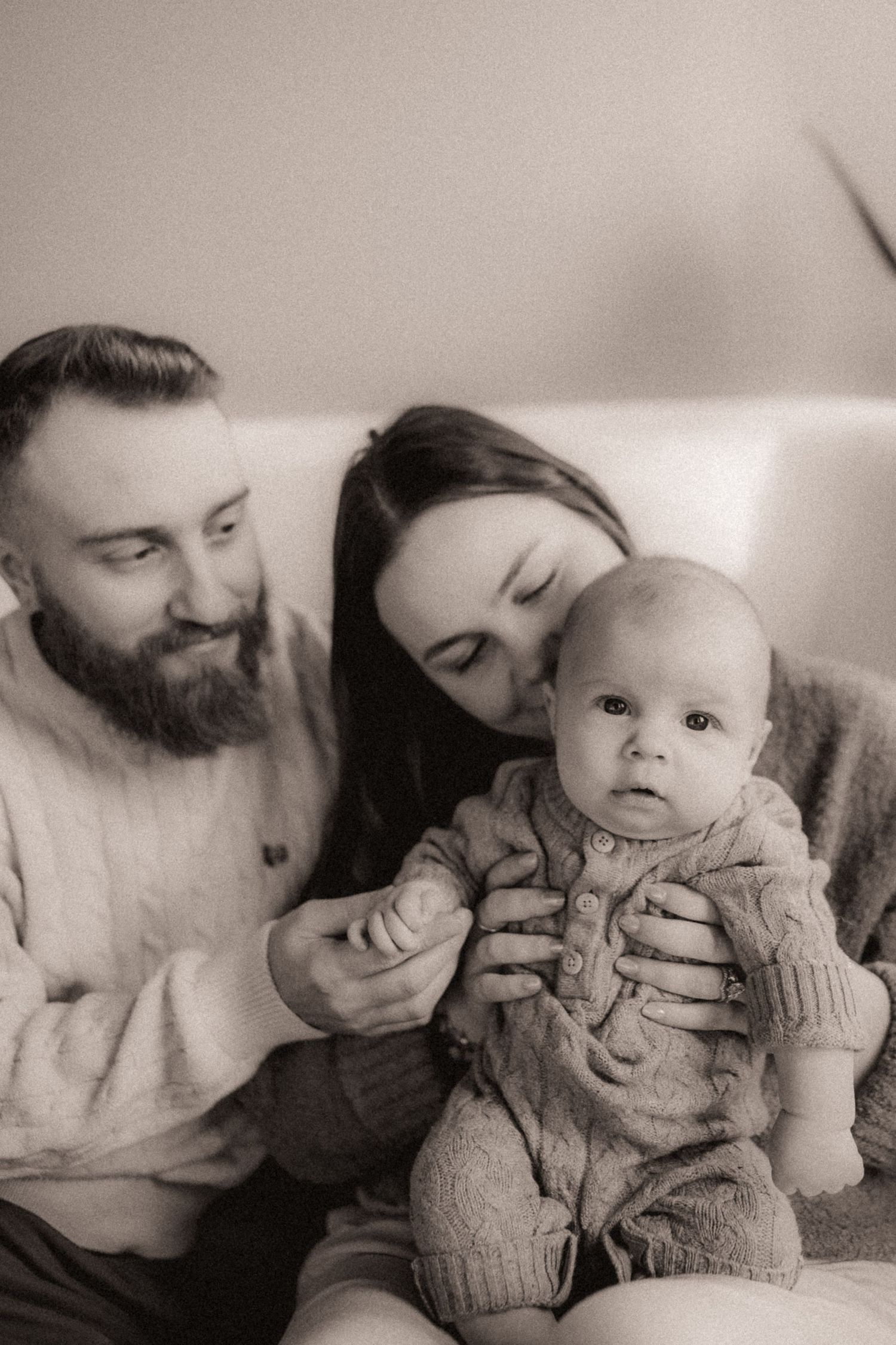 Black and white family portrait series showing gentle moments with a baby in a knit sweater.