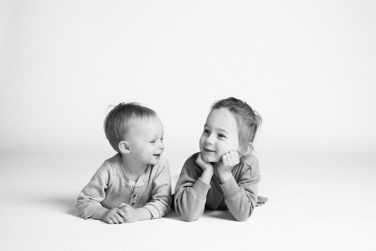 Black and white image of babies lying side by side on a white background, showing joyful expressions.