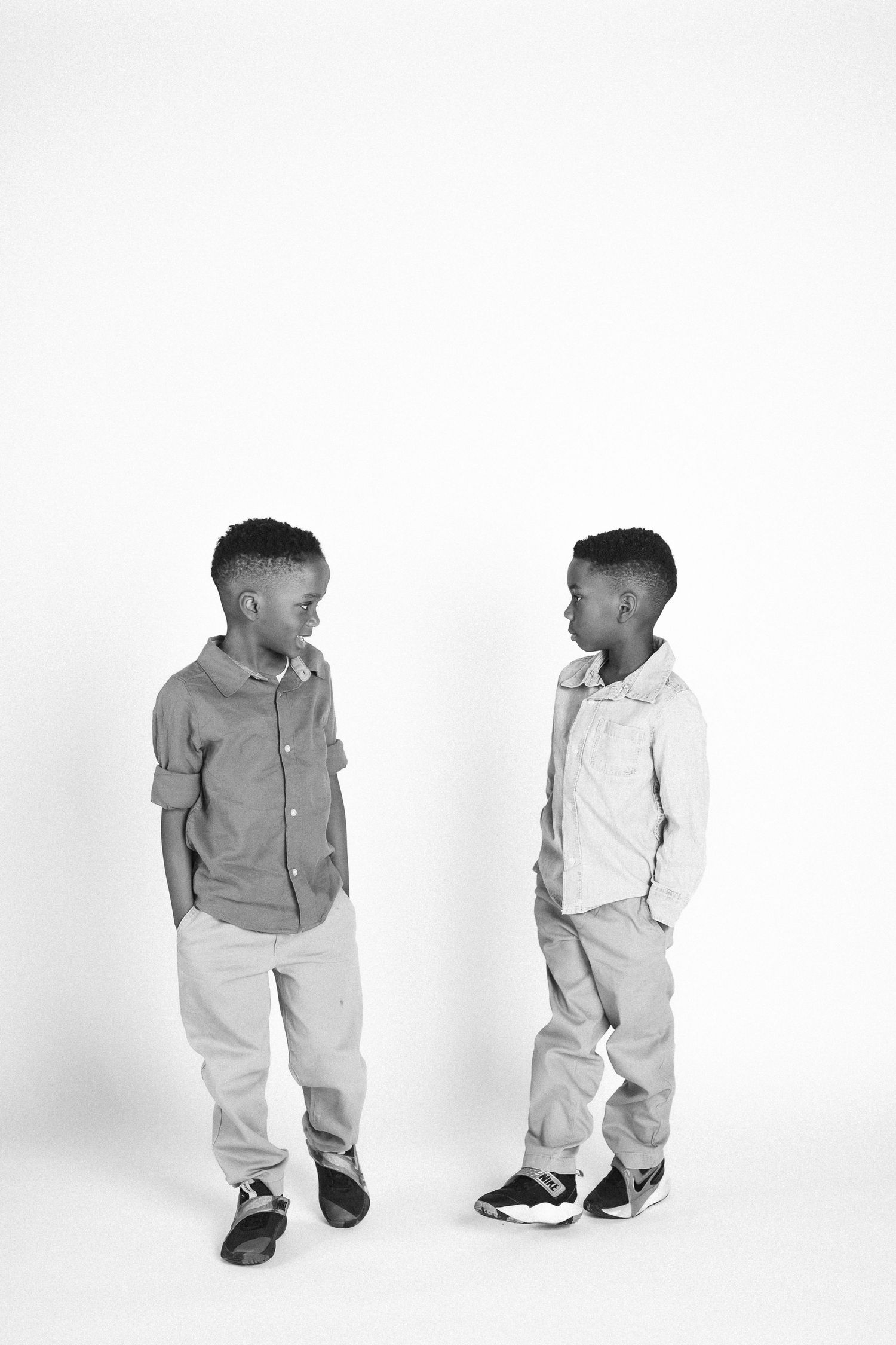 Two children in casual outfits walk and play together in a white studio setting.