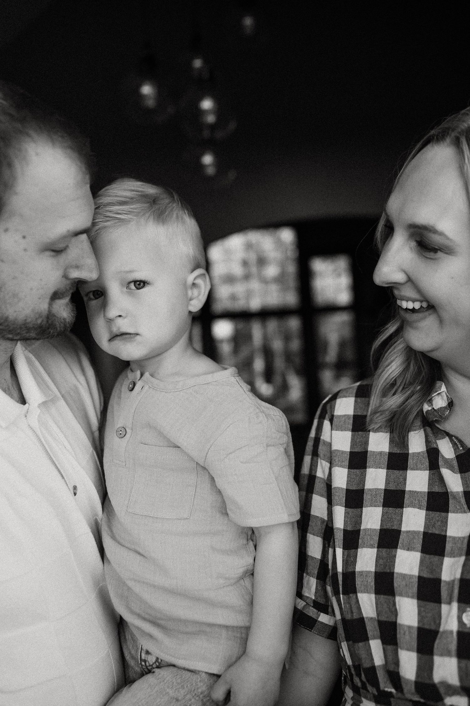 Black and white portrait of parents with young blond toddler boy indoors.