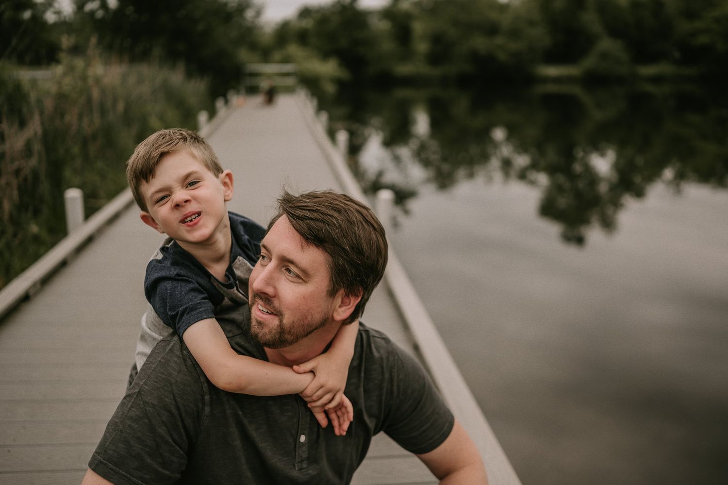 A heartwarming moment captured on a wooden boardwalk over a peaceful lake at sunset.