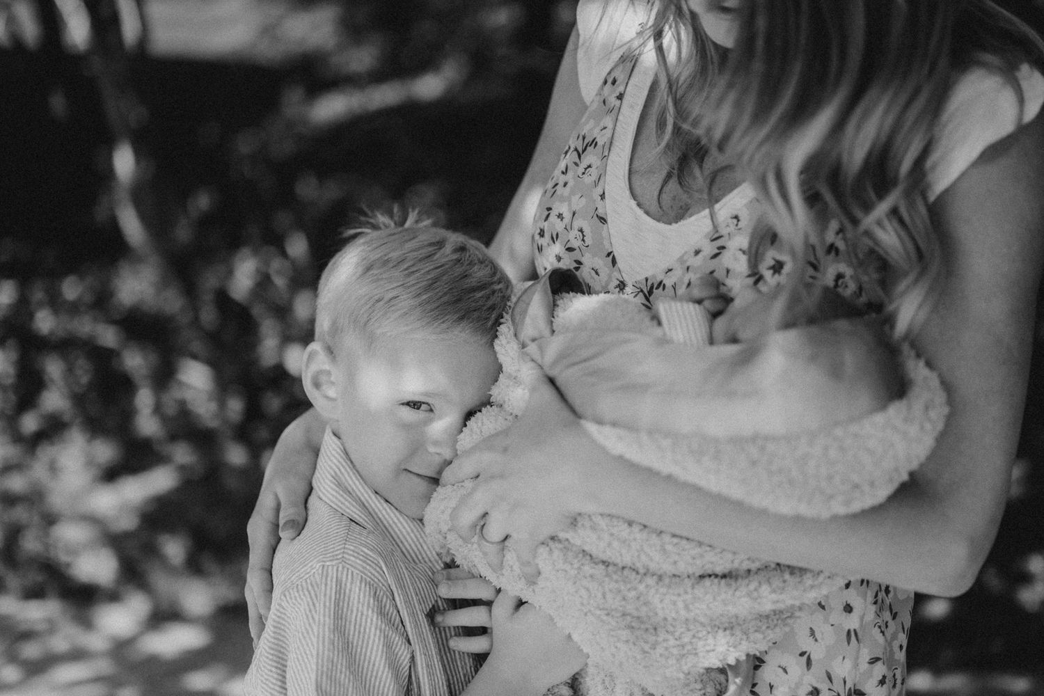 Black and white intimate family moment captured under spring foliage.