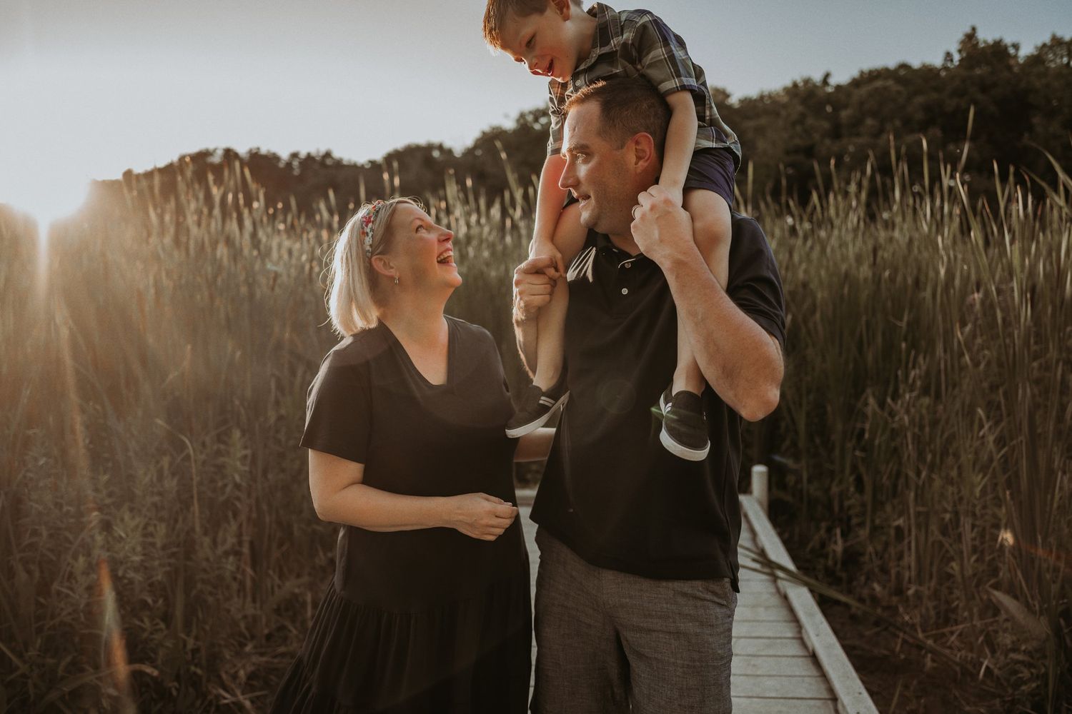 Family enjoying a sunset moment together on a wooden boardwalk through tall grass.