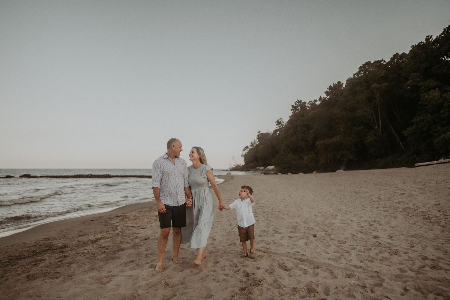 A family portrait on the beach at sunset with wooded cliffs in the background.