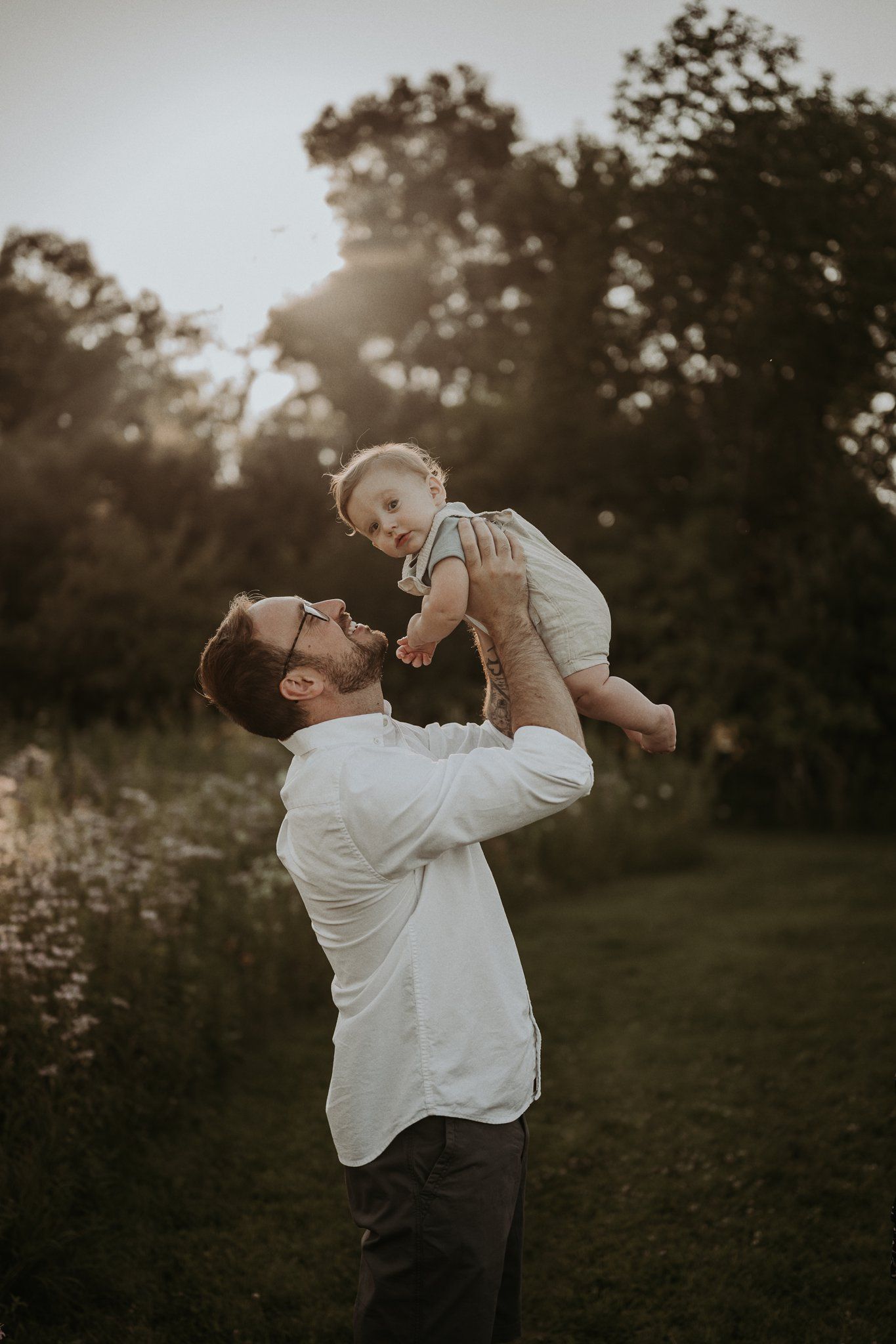 Joyful sunset moment as adult lifts small child in the air outdoors.