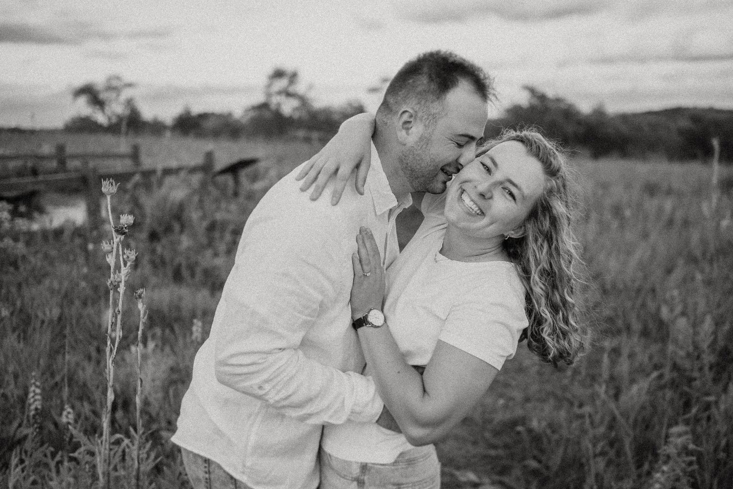 A black and white portrait capturing a couple's laughter in a rural field setting.