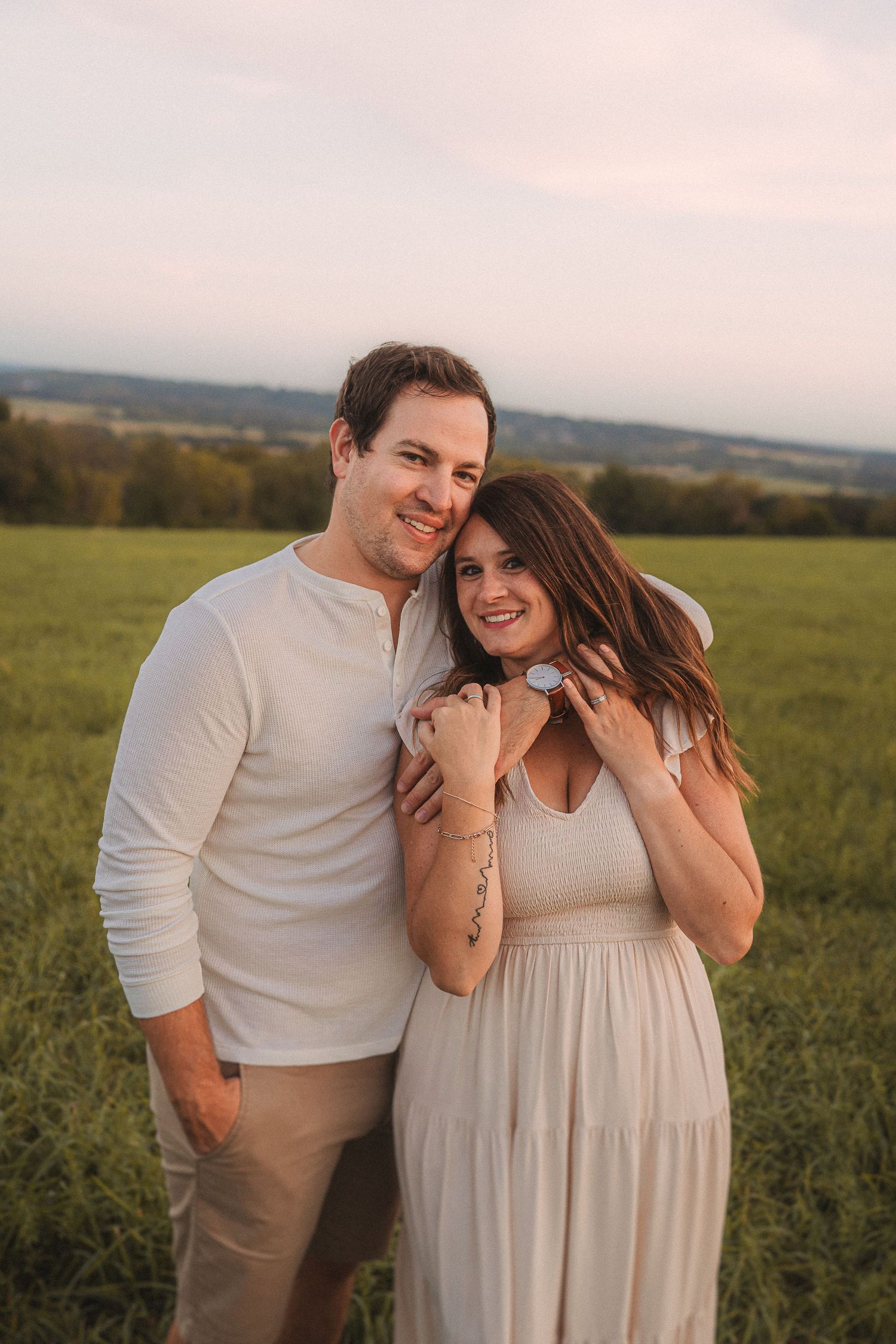 Romantic sunset portrait of couple in coordinating white outfits standing in grassy field.
