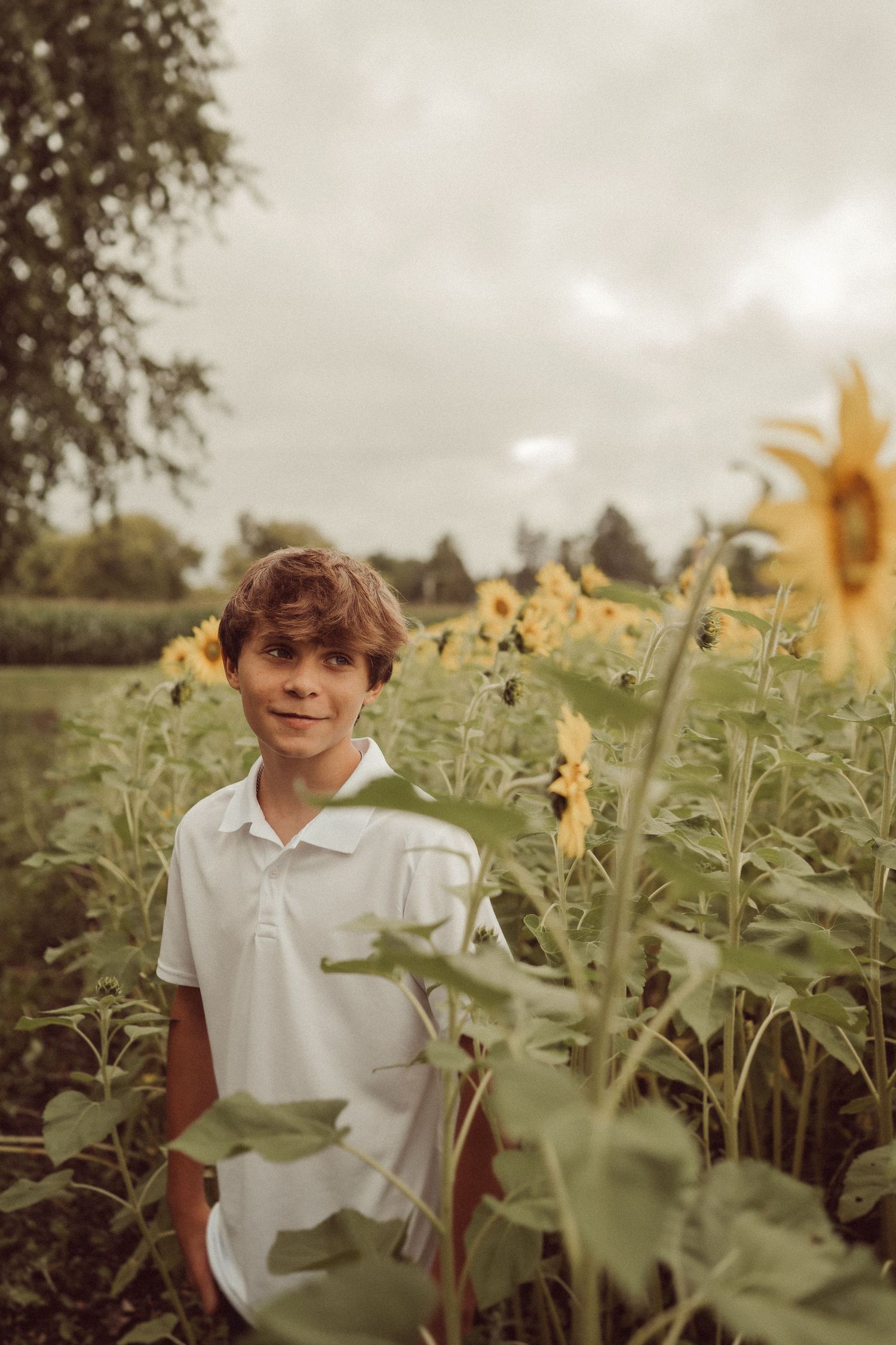 A candid portrait in a sunflower field with soft natural lighting and cloudy skies.