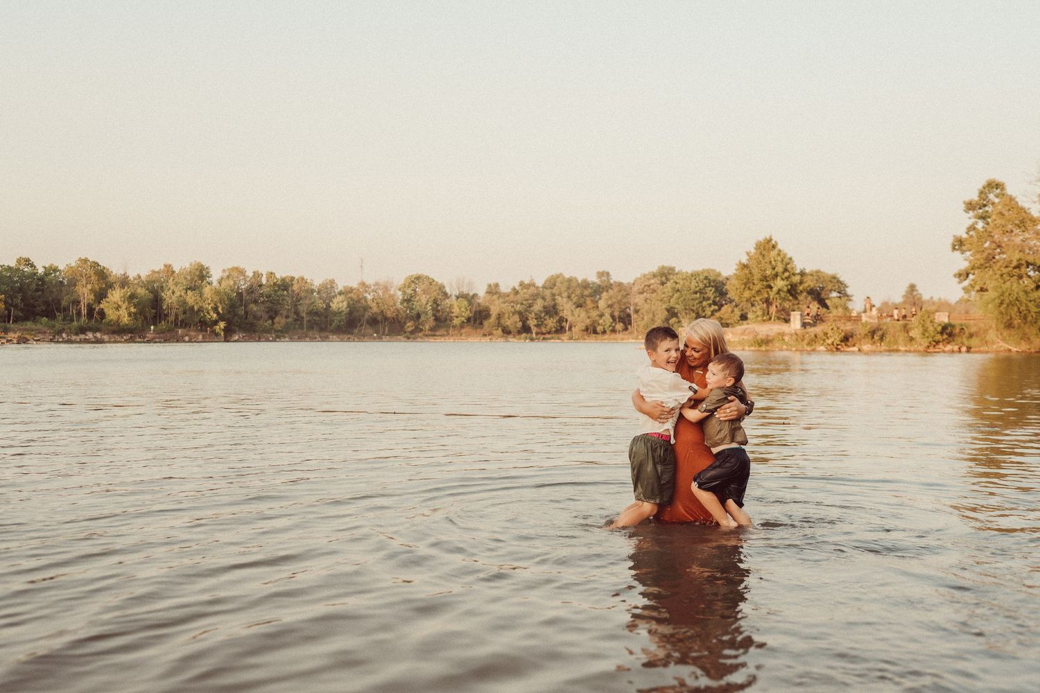 Family plays together in waist-deep water during golden hour on a serene lake.