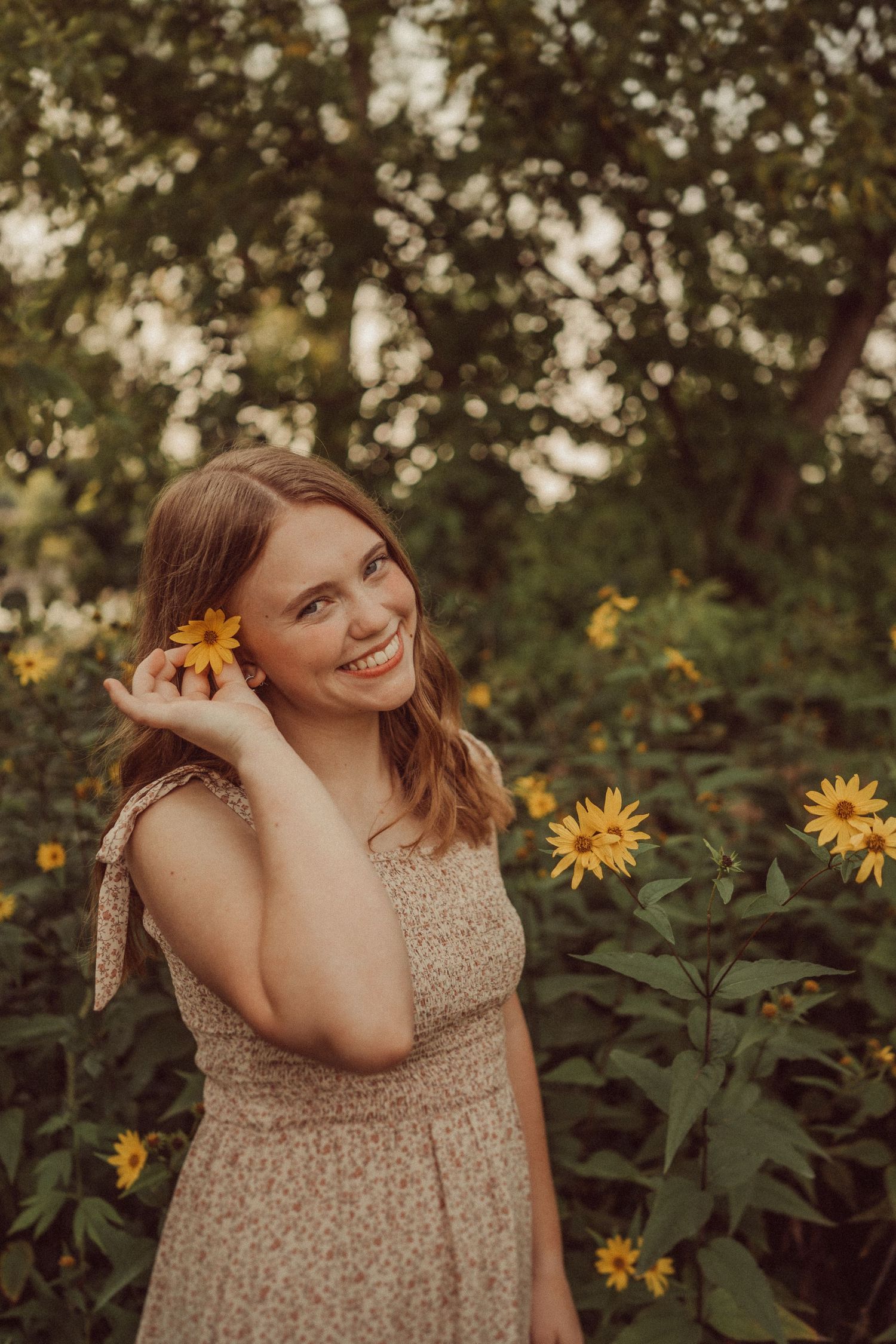 A dreamy summer portrait with sunflowers and warm golden light filtering through trees.