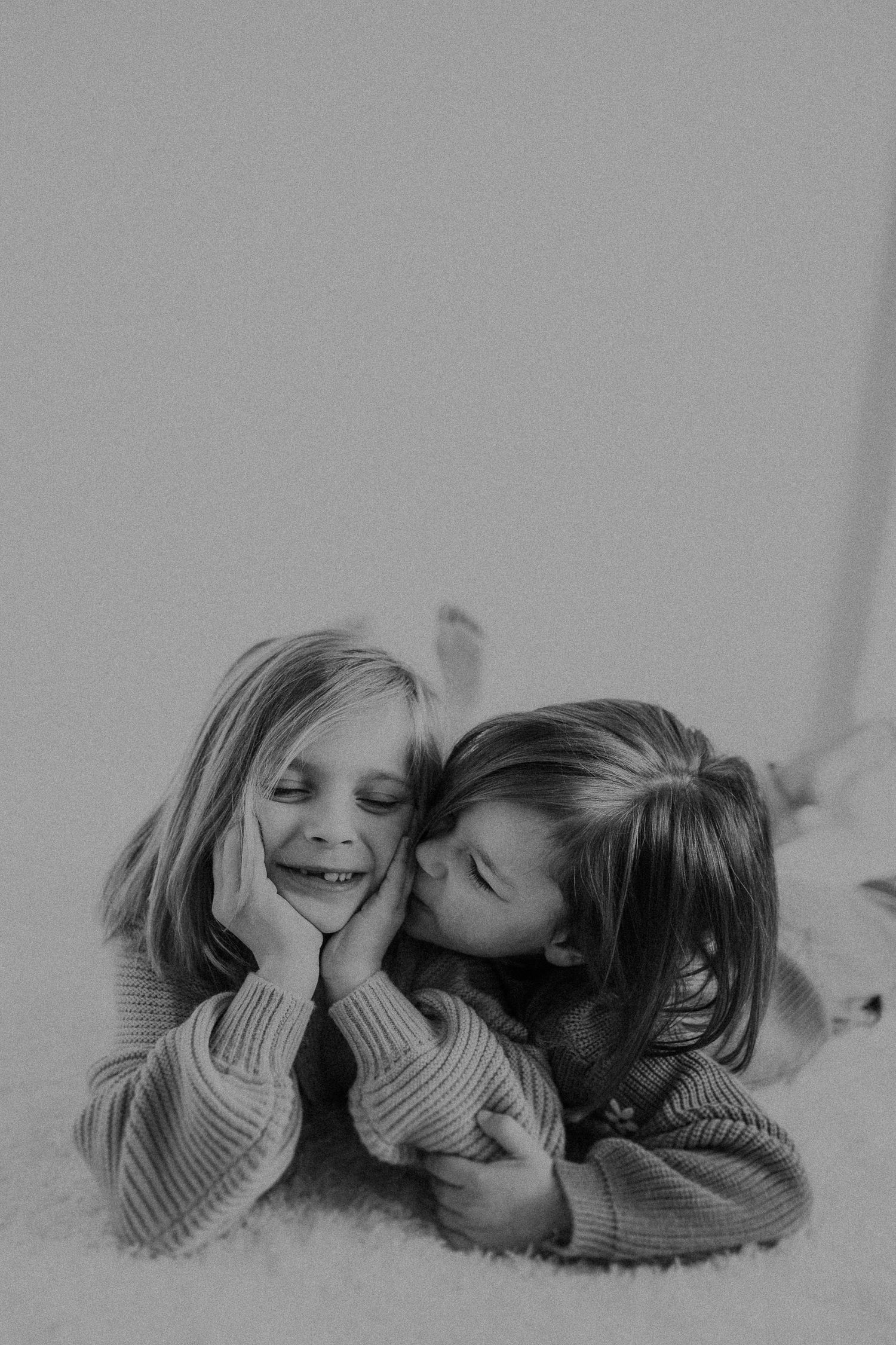 Two young people in cozy sweaters share a sweet moment of laughter on white carpet.