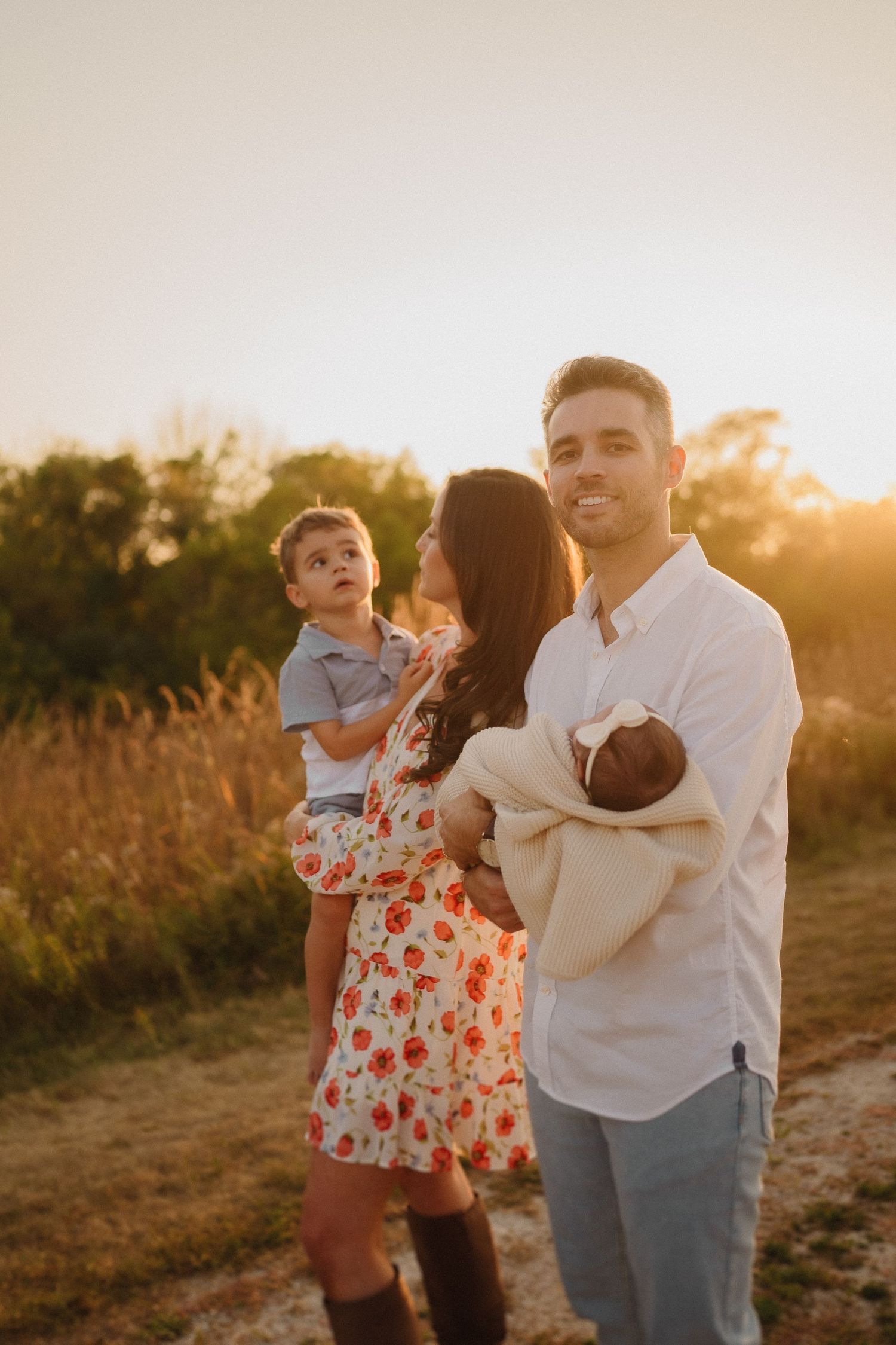 Tender family portrait with newborn baby captured in warm sunset light on a rural path.