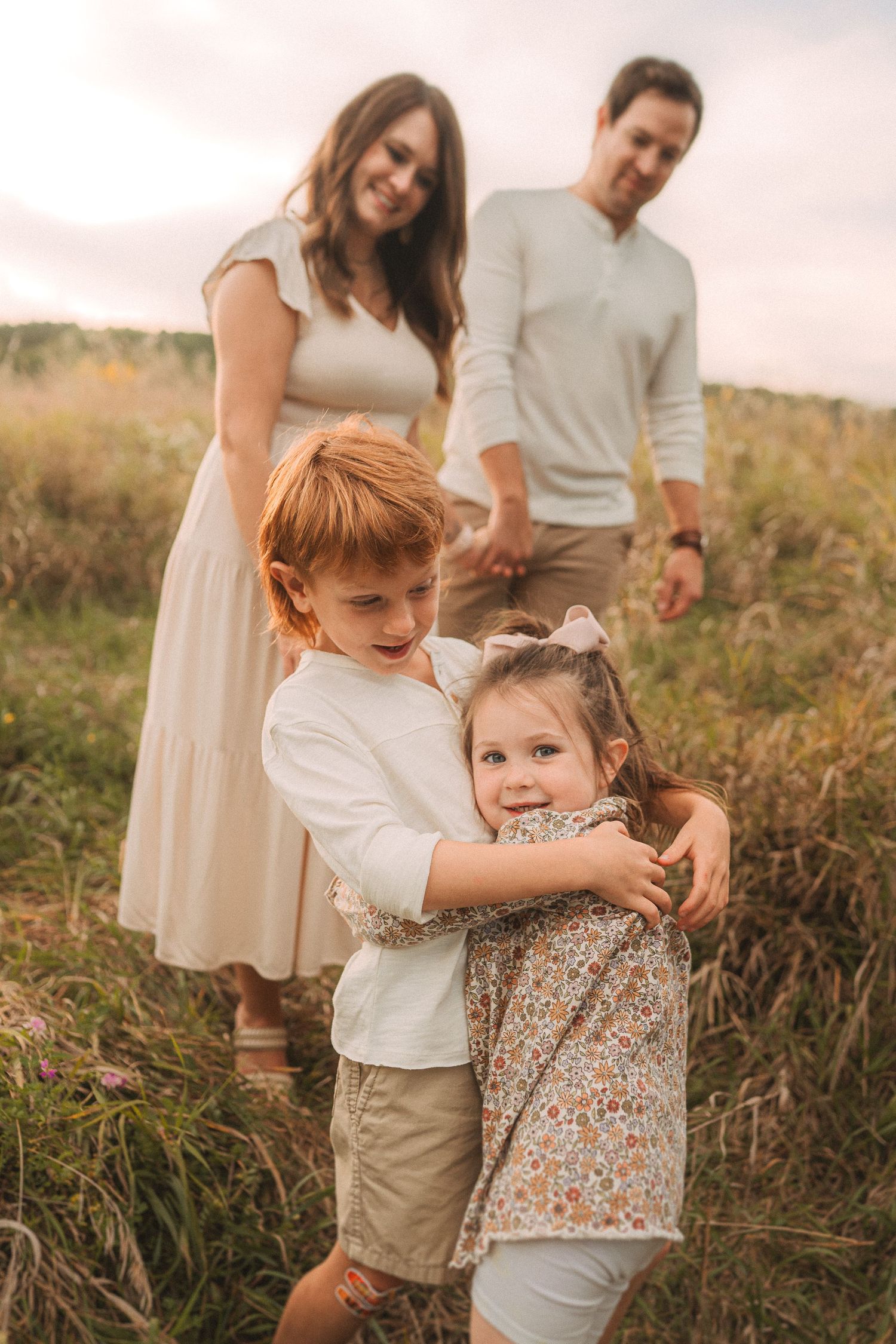 Family shares tender moment together in field during golden hour.