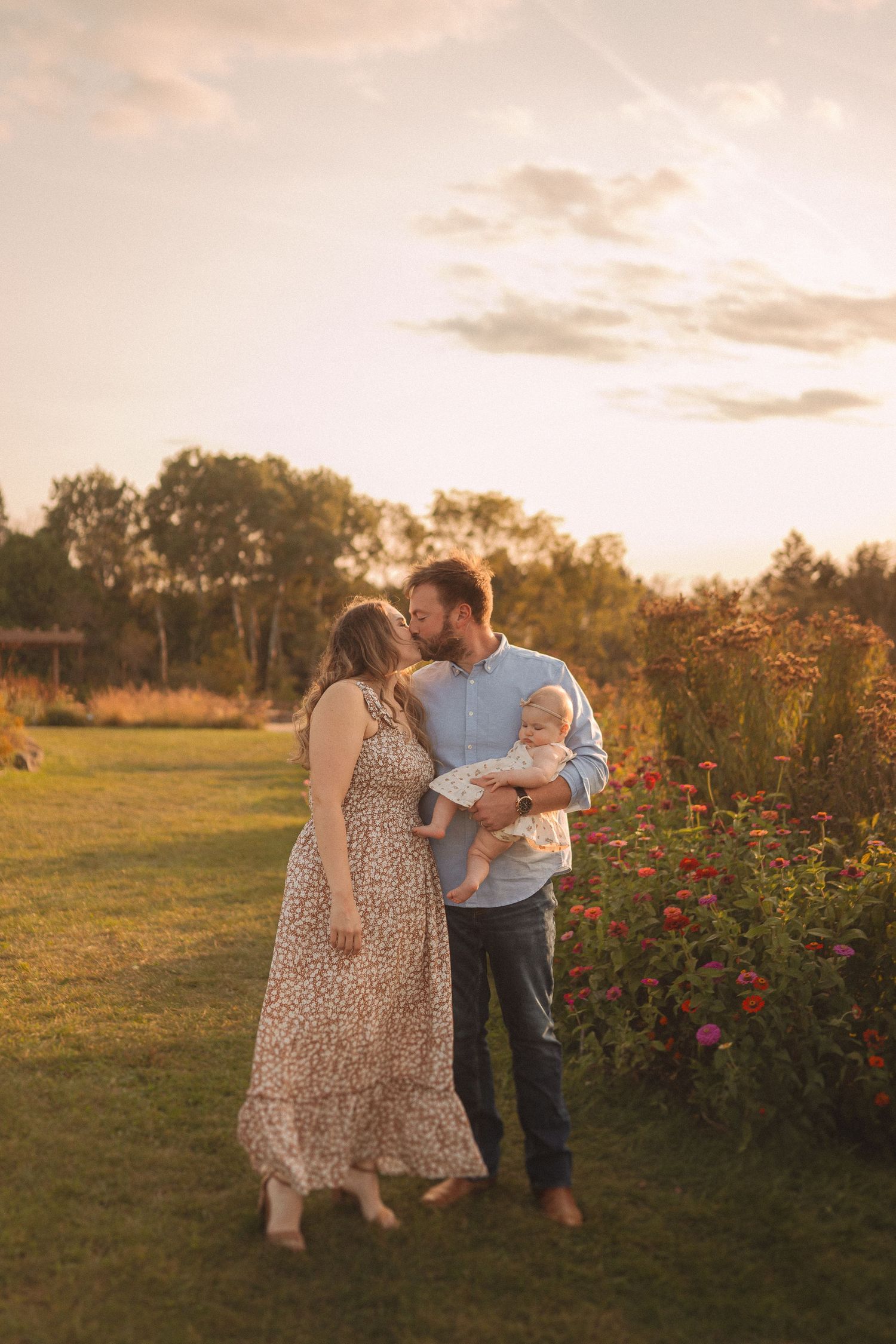 Family shares intimate moment during sunset photoshoot in garden with red flowers.