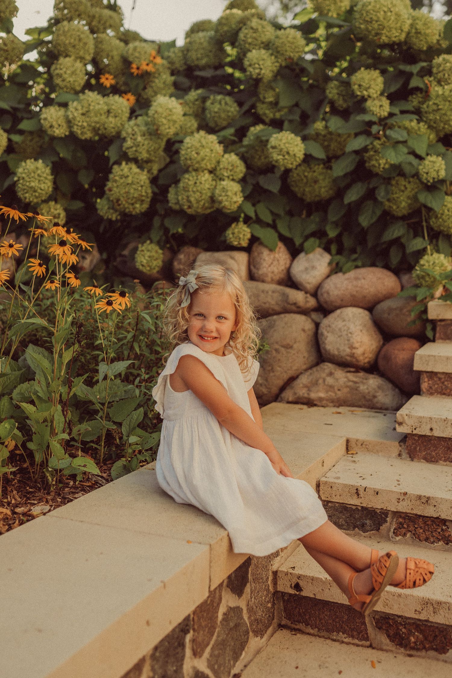 Stone steps in a garden with raised beds featuring lush hydrangeas and orange flowers in summer.