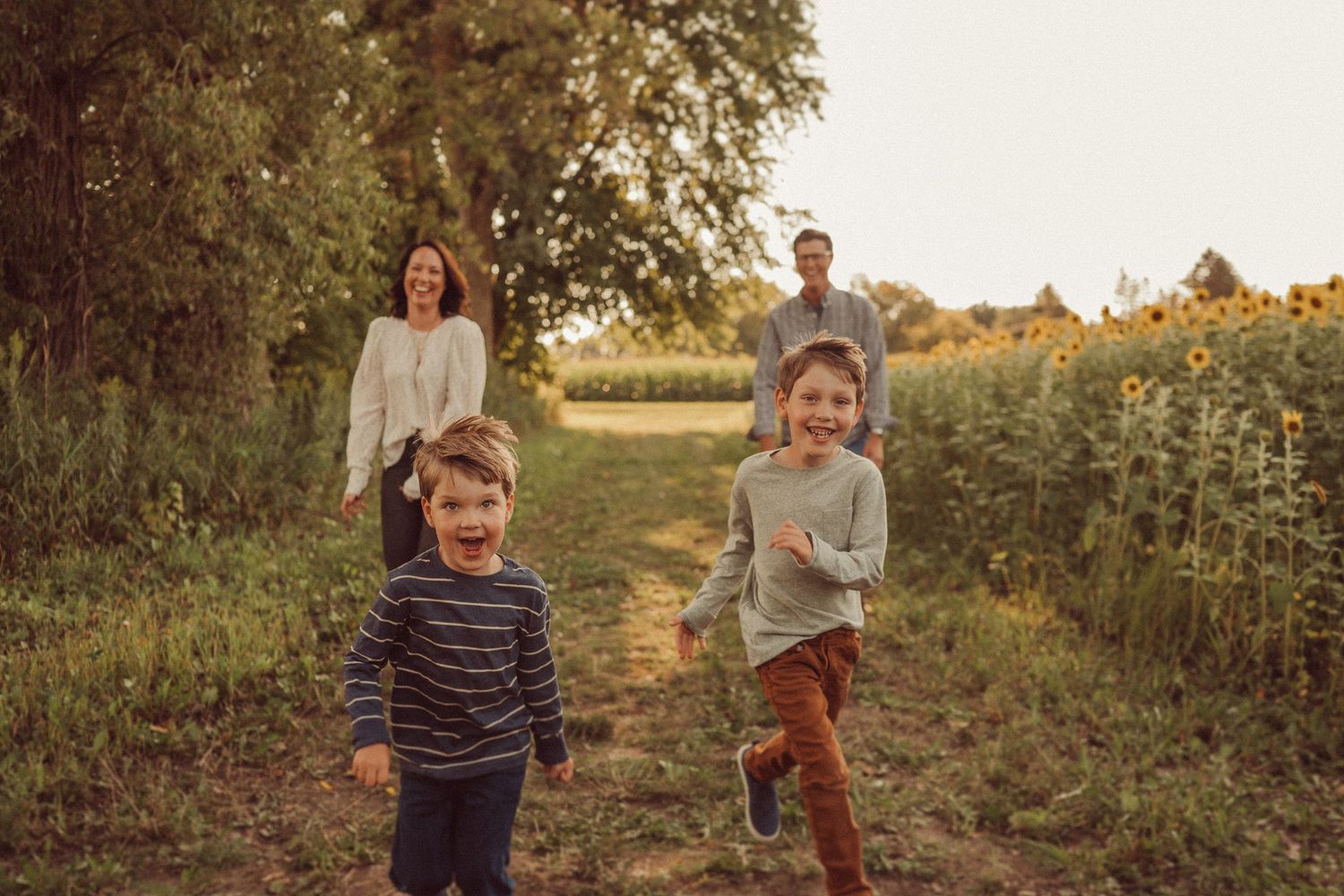 Children running joyfully along a path near sunflowers during golden hour.