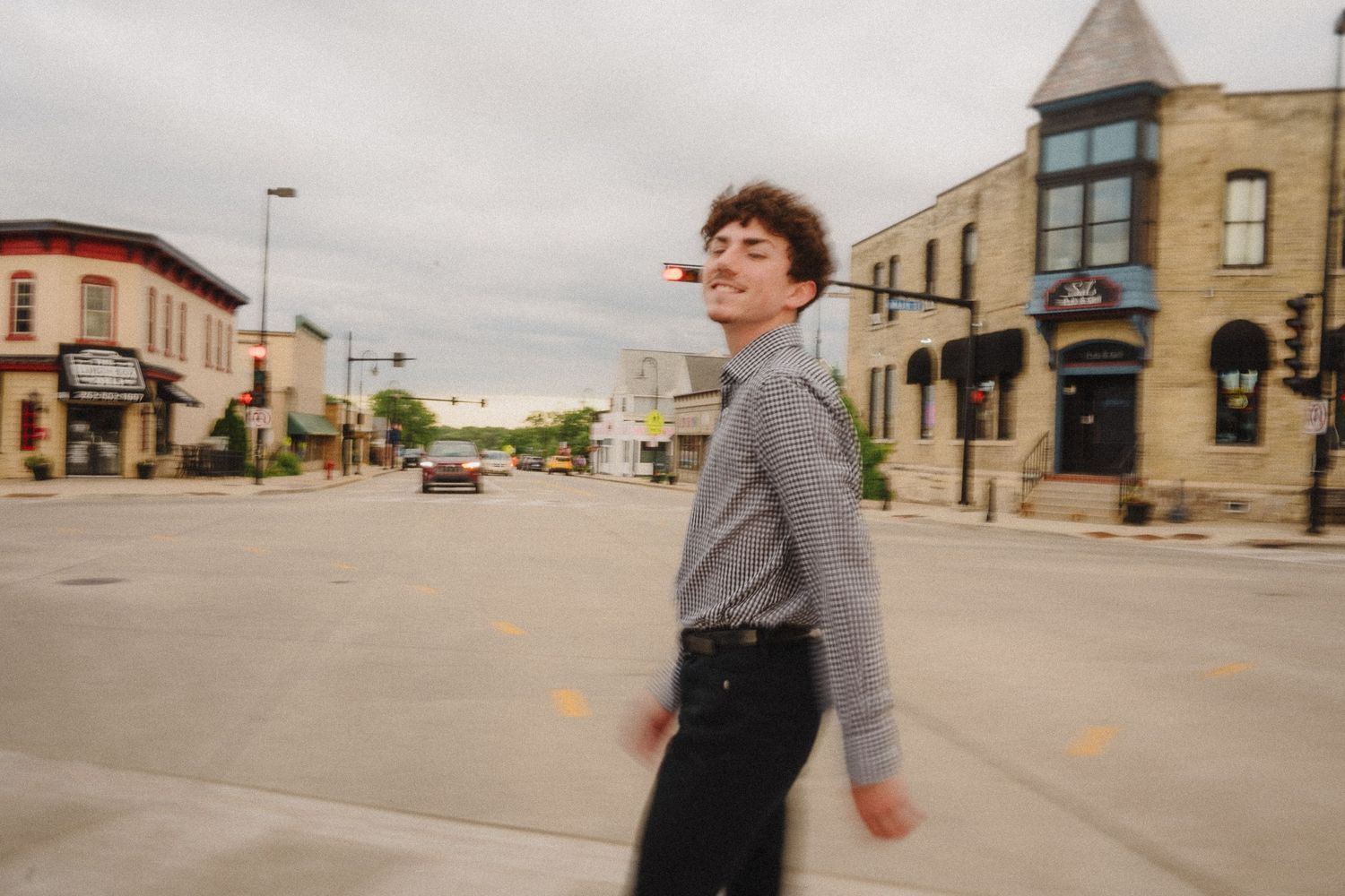A person in casual attire walks along a small town street with brick buildings in the background.