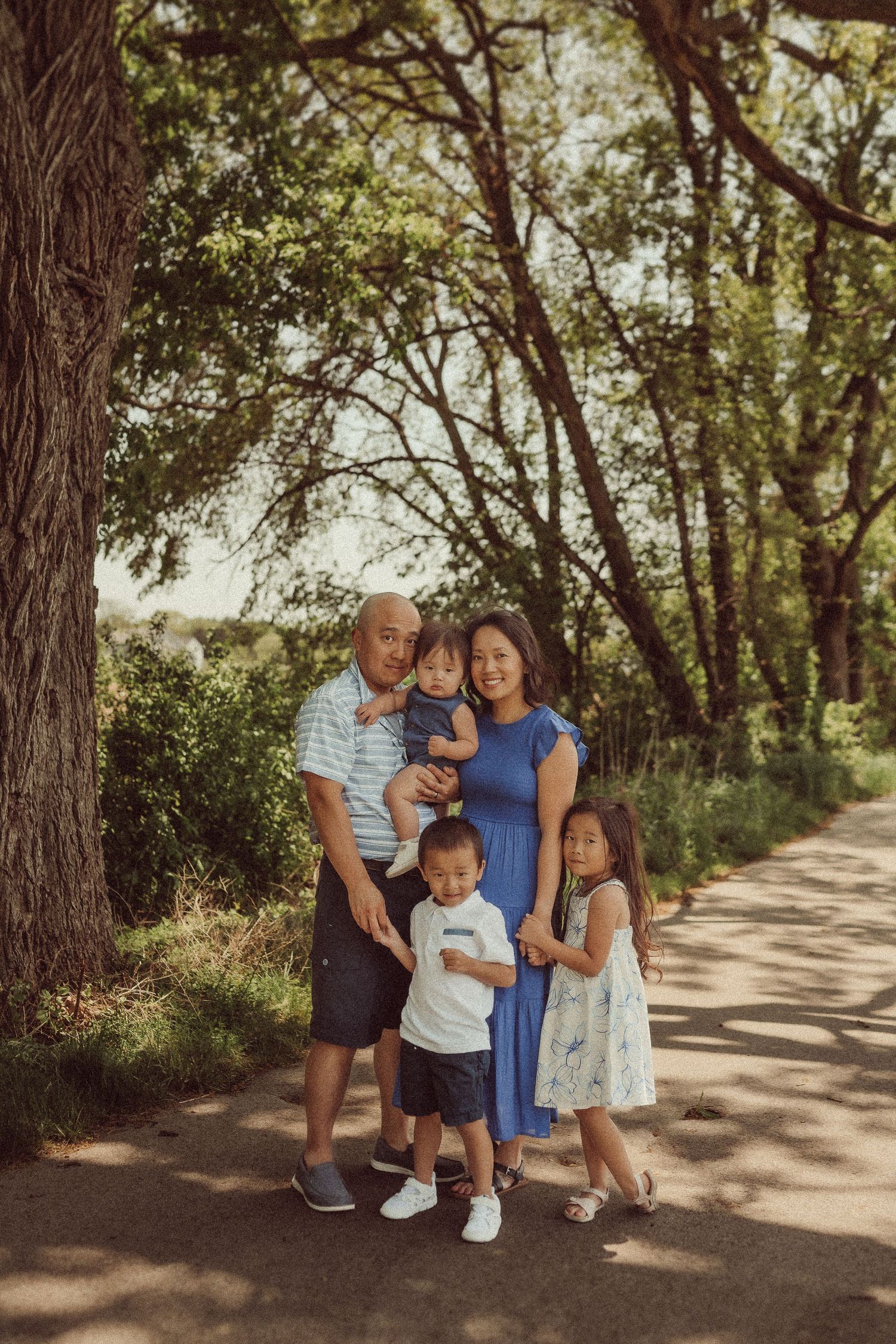 Family gathered for a portrait under majestic trees on a winding path.