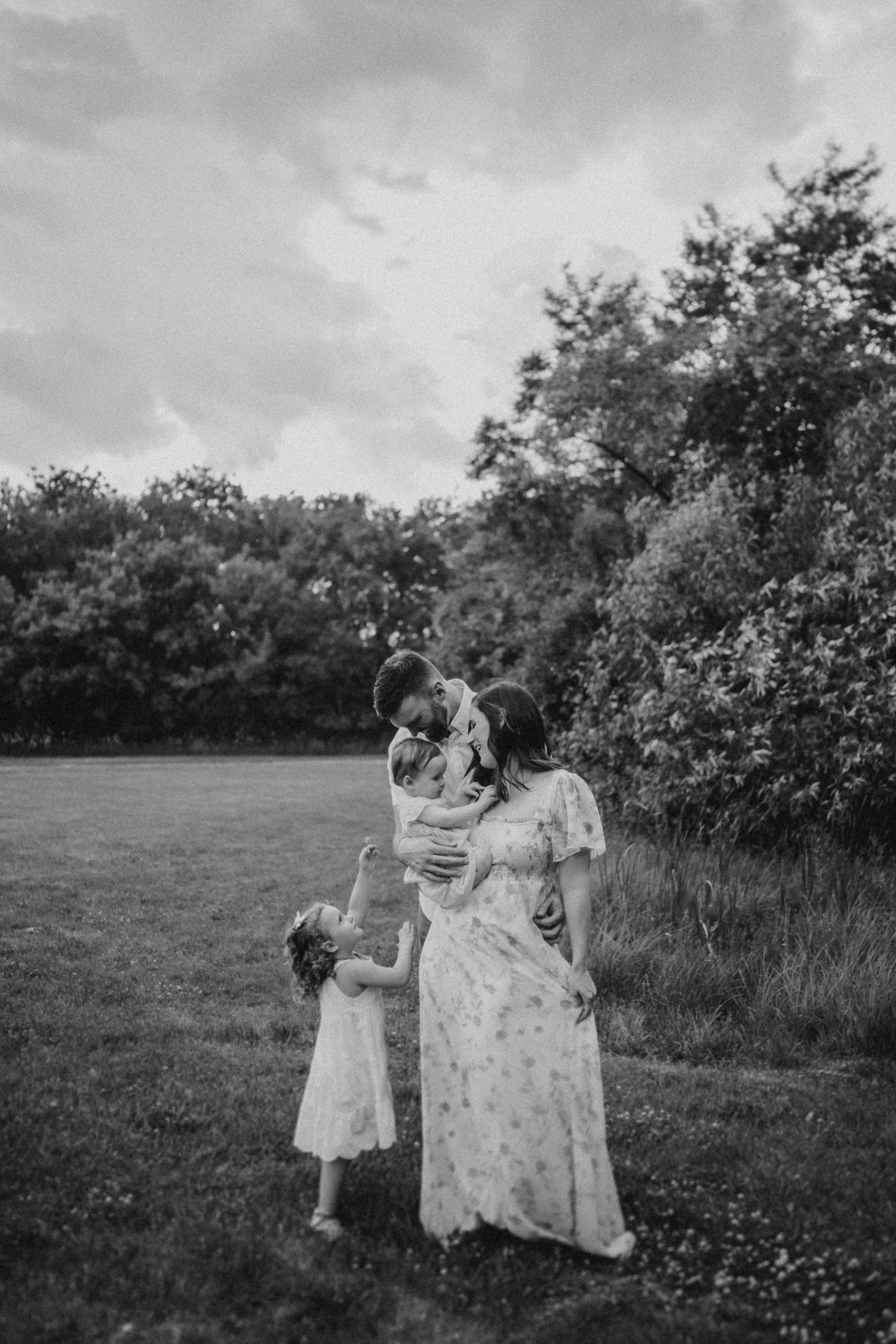 A black and white family portrait captured in a serene outdoor setting.