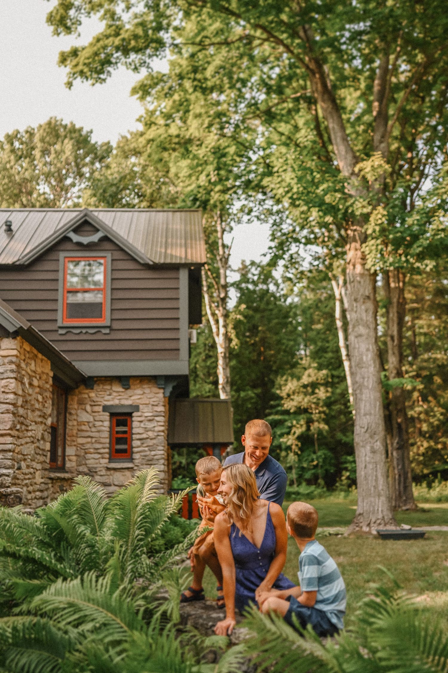 Candid family photo with rustic stone house and lush ferns in background.