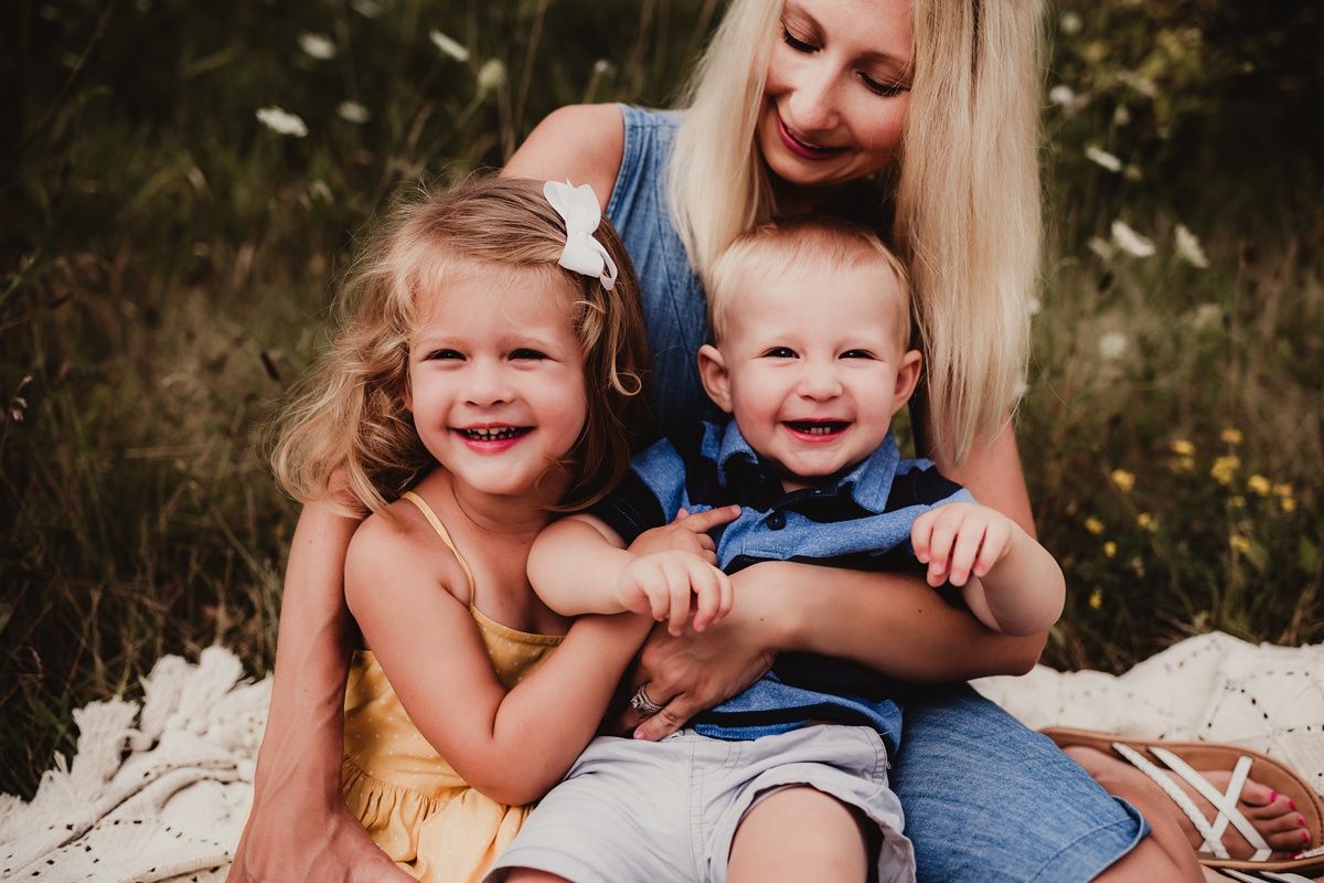 Candid outdoor family portrait with everyone laughing together on a white blanket.