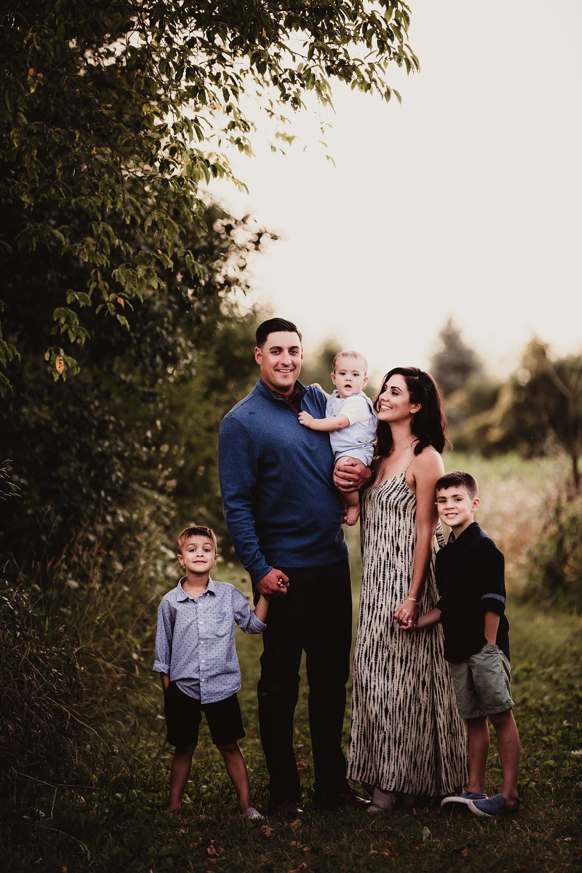 Family portrait on nature path with parents and children in coordinated casual outfits.