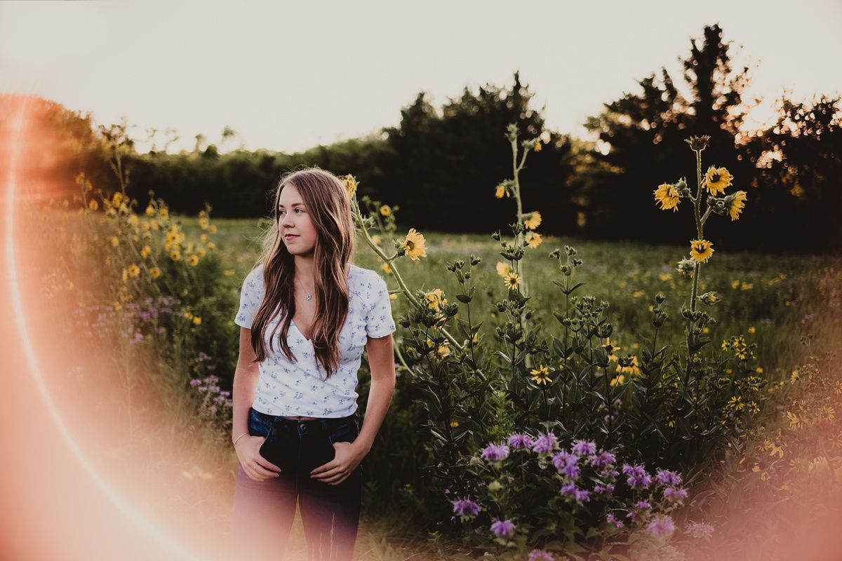 Dreamy outdoor portrait with lens flare and purple flowers in foreground.