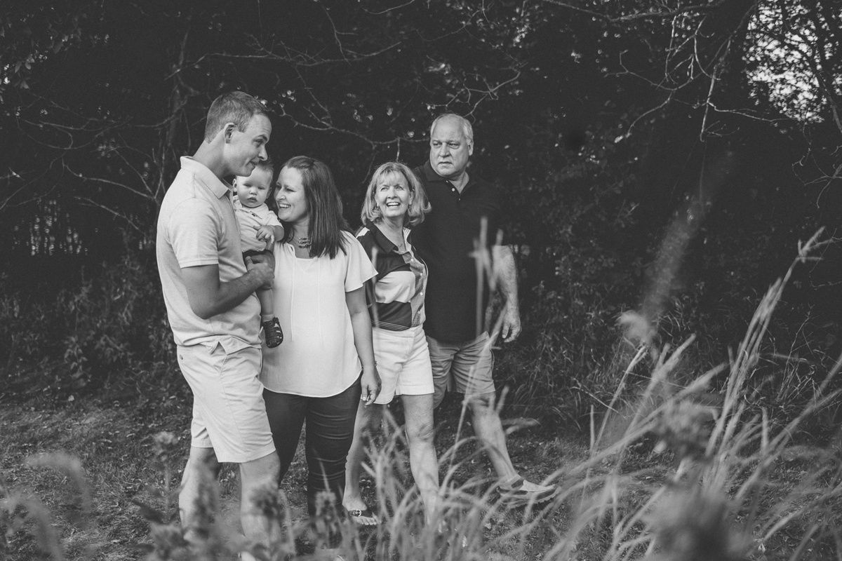 Black and white group photo of people standing together in tall grass with trees in background.