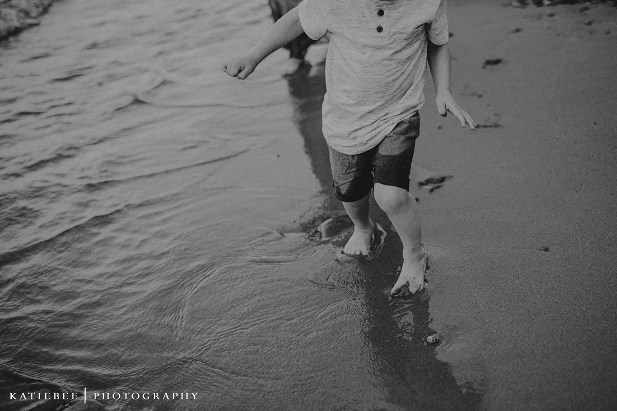 Black and white photo of splashing feet walking along the water's edge at the beach.