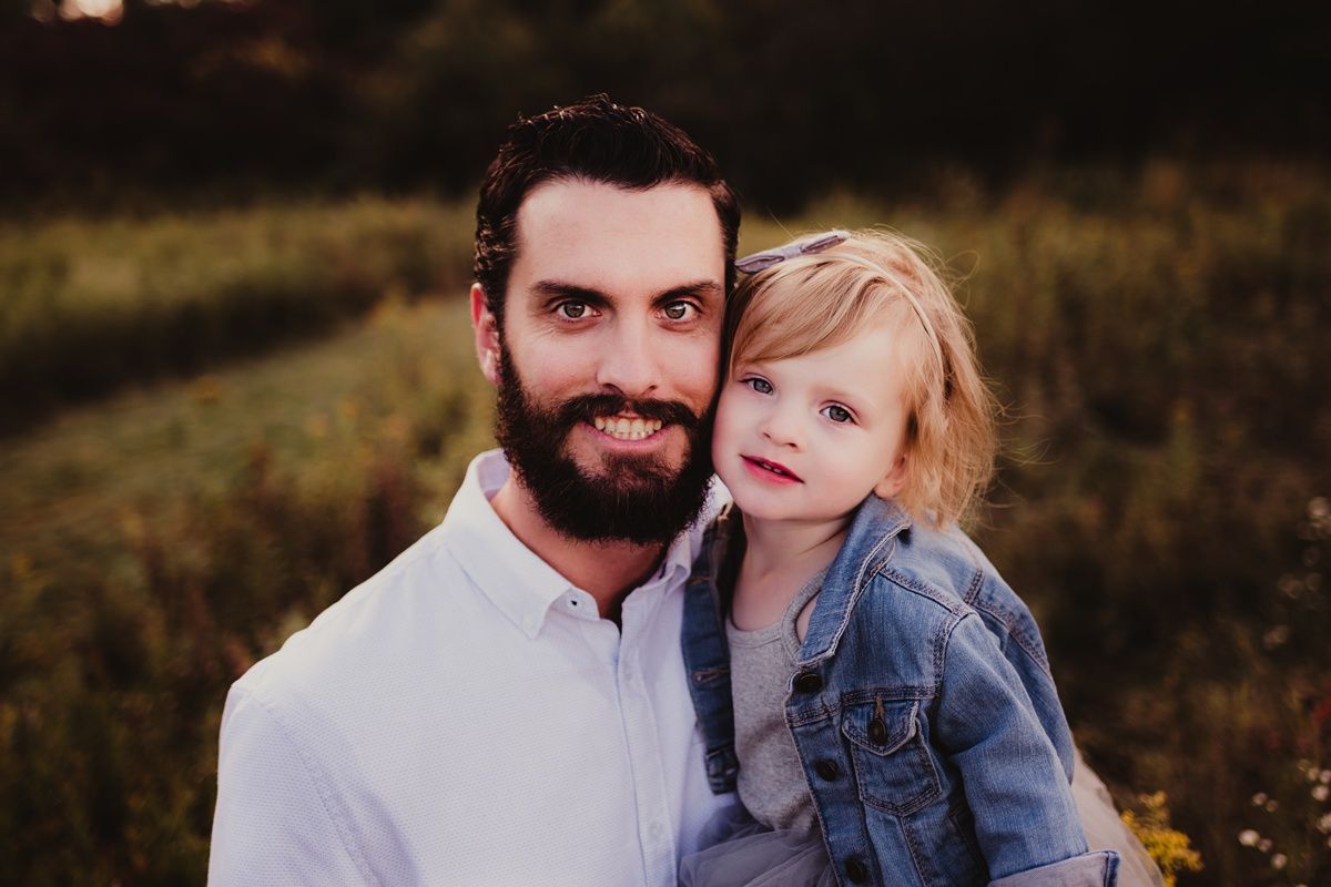 Outdoor portrait of parent and child in casual attire against a natural sunset background.
