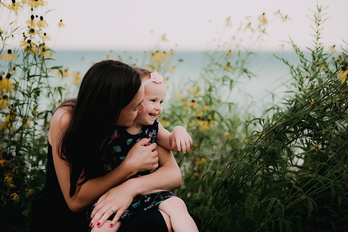 A tender moment between parent and child amongst yellow wildflowers by the ocean.