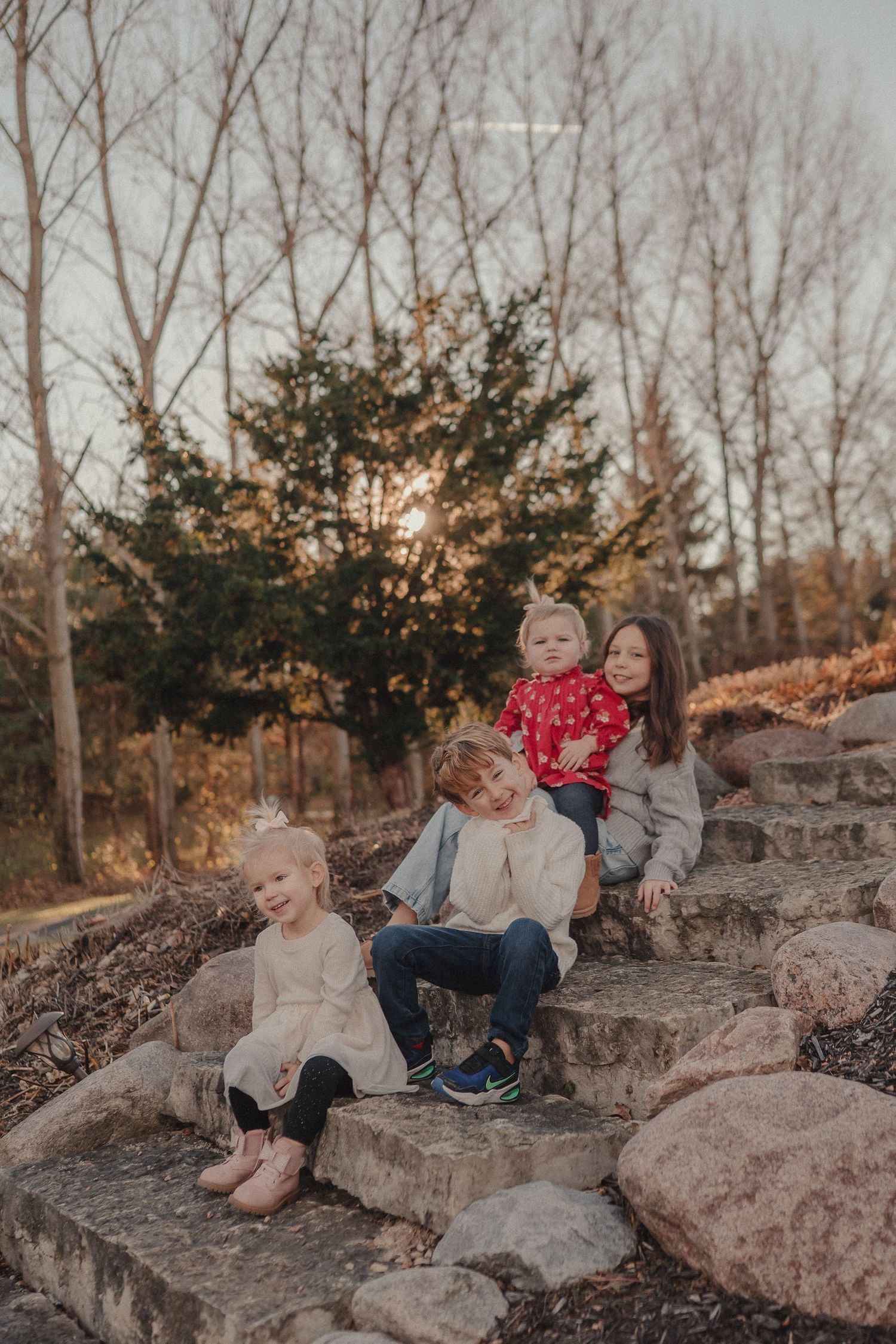 Family members sitting on large rocks during golden hour with bare trees in the background.